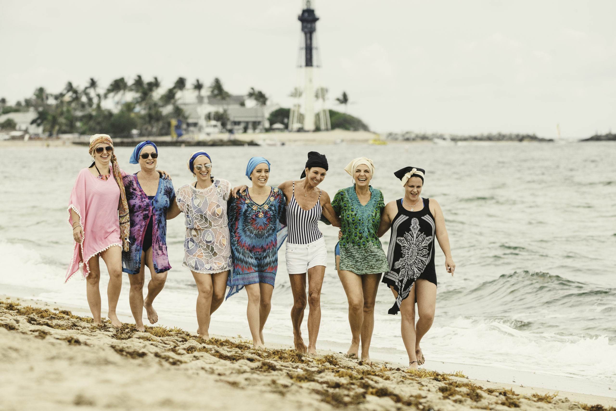 Group of seven women walking along the beach by the water all smiling