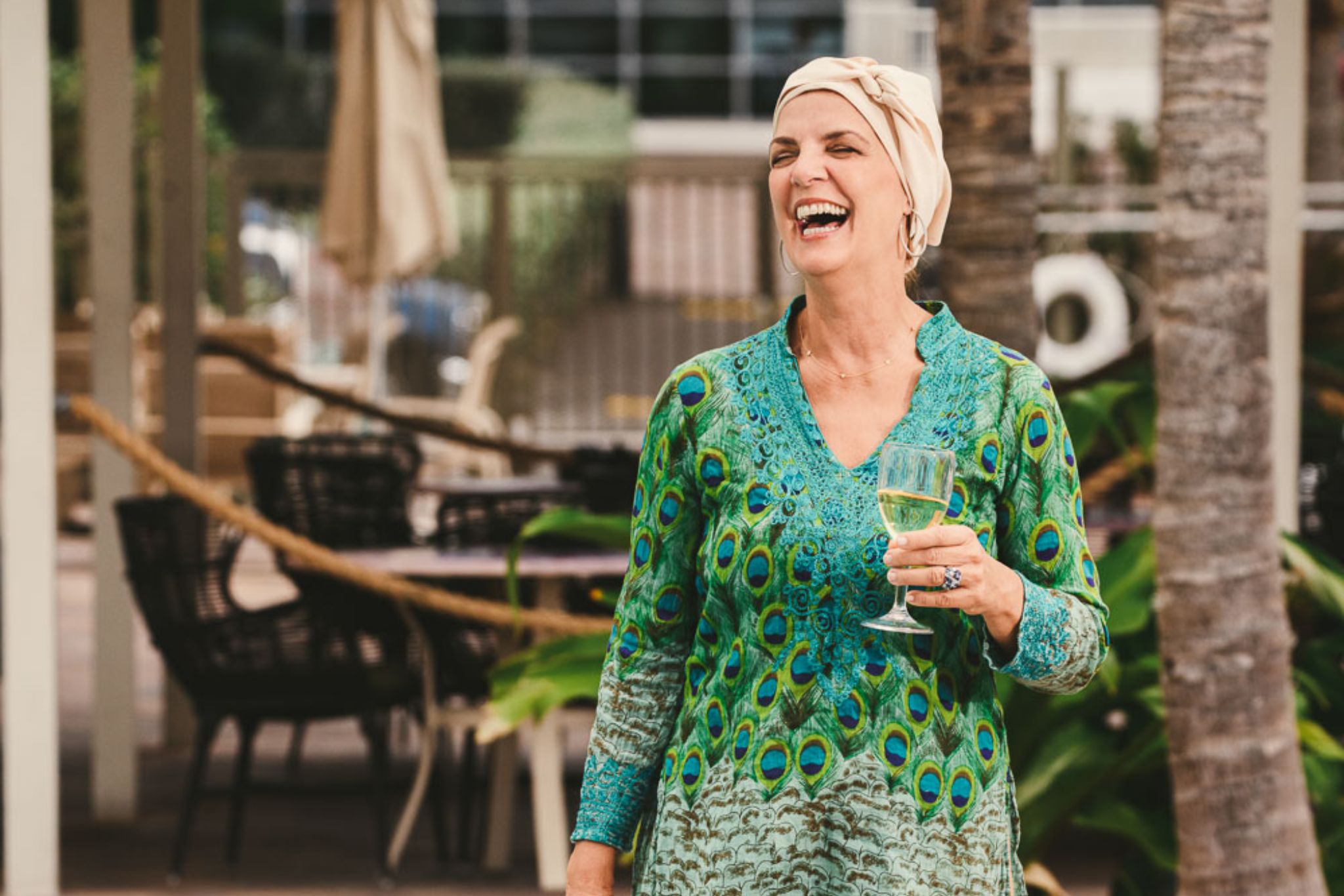 Woman wearing a peacock patterned outfit holding a glass of wine laughing