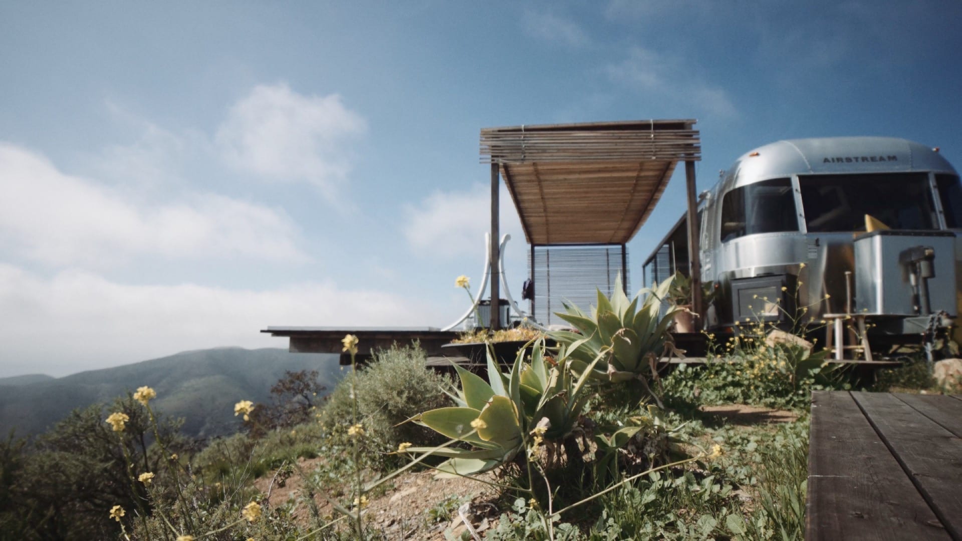 View of a silver colored RV with a temporary patio overlooking a valley.