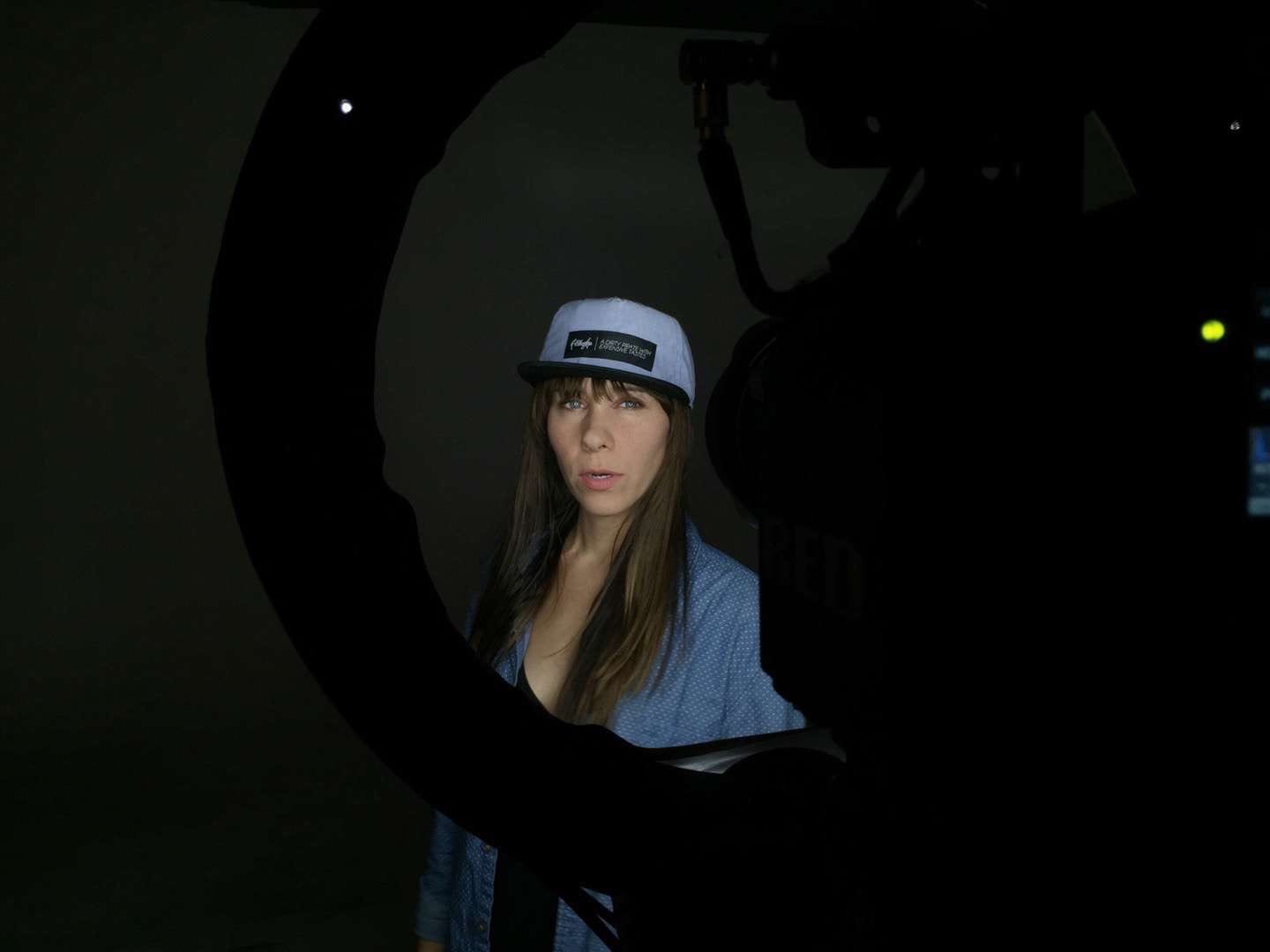 Filibuster Apparel Woman with long brown hair in a blue shirt wearing a light blue hat with black rim by video equipment