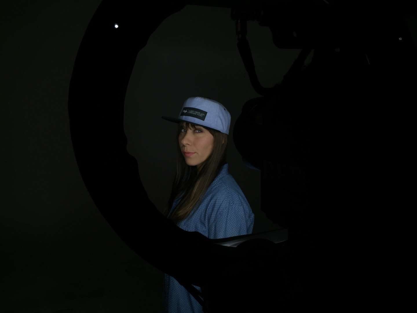 Filibuster Apparel Woman with long brown hair in a blue shirt wearing a light blue hat with black rim by video equipment