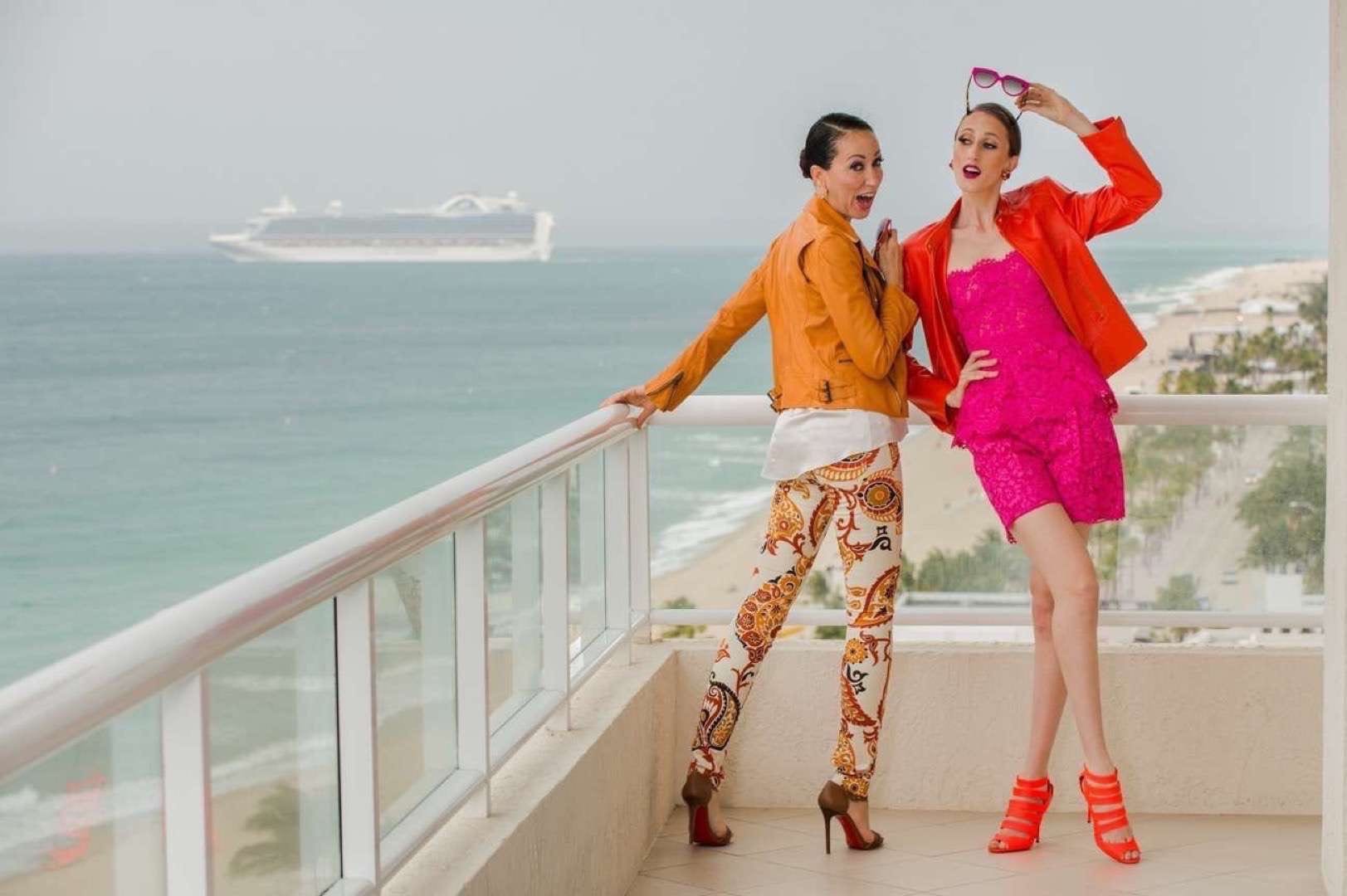 Las Olas Magazine Pat and Anna Cleveland Two women in orange and hot pink outfits posing for camera on a balcony with a cruise ship in the background