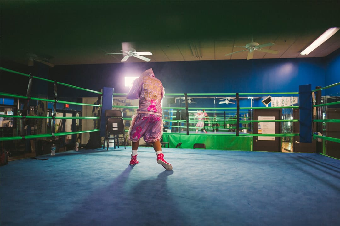 Female boxer in pink outfit facing away from the camera warming up with boxing moves.