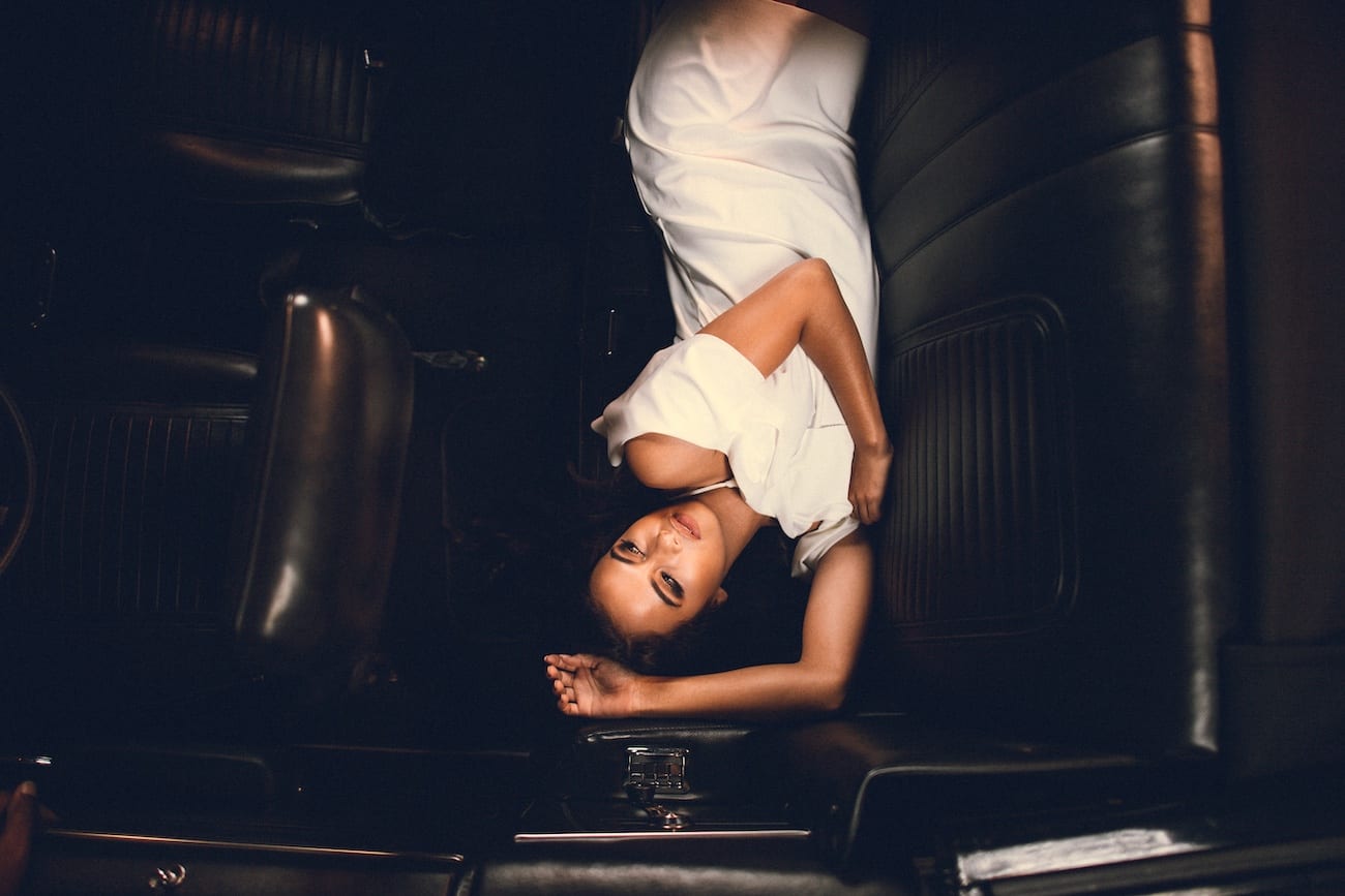 South Florida Studio Rentals Headshot of woman laying across the back seat of a car in a white dress posing for camera