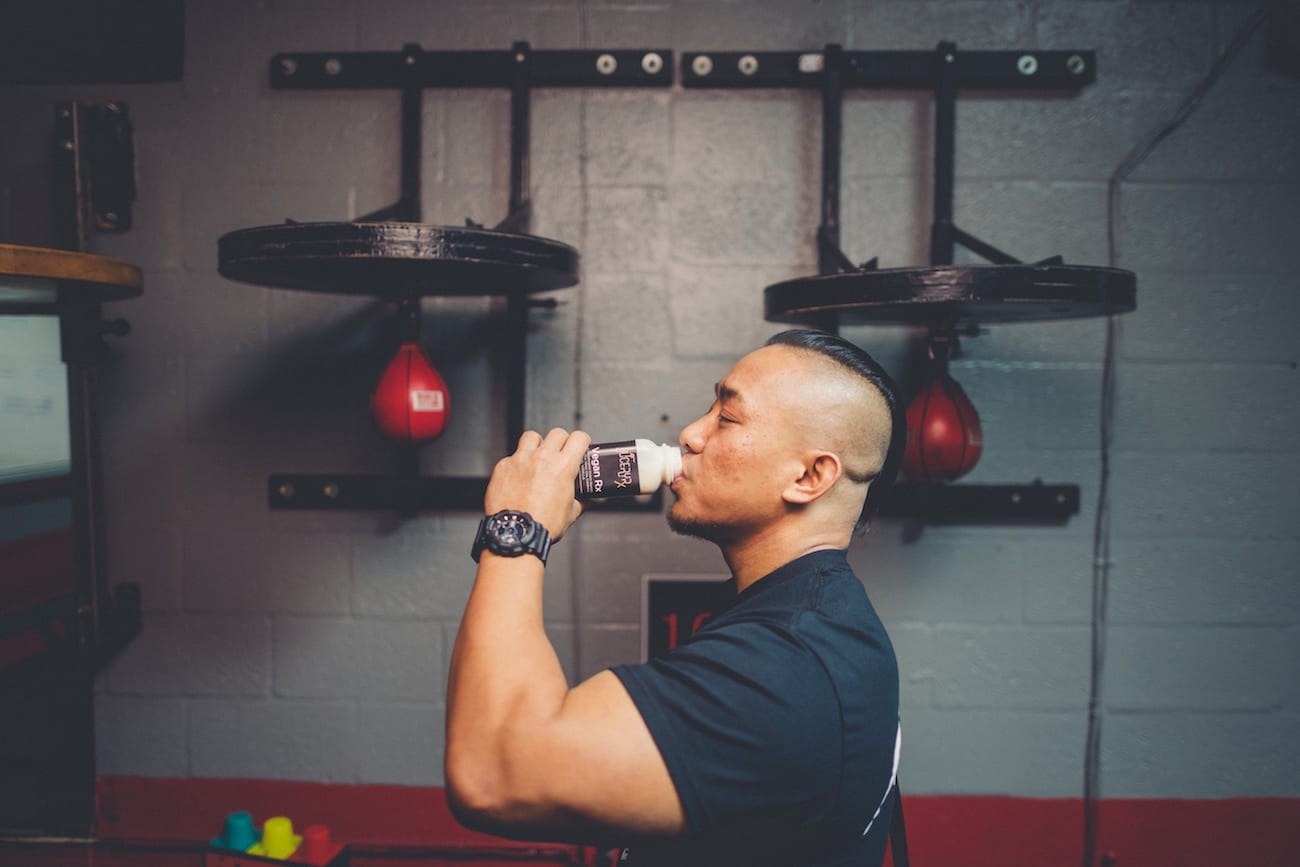 Muscular man drinking Vegan Rx from plastic container in a gym