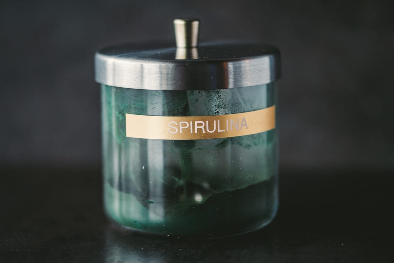 Spirulina powder in a glass container with a scoop