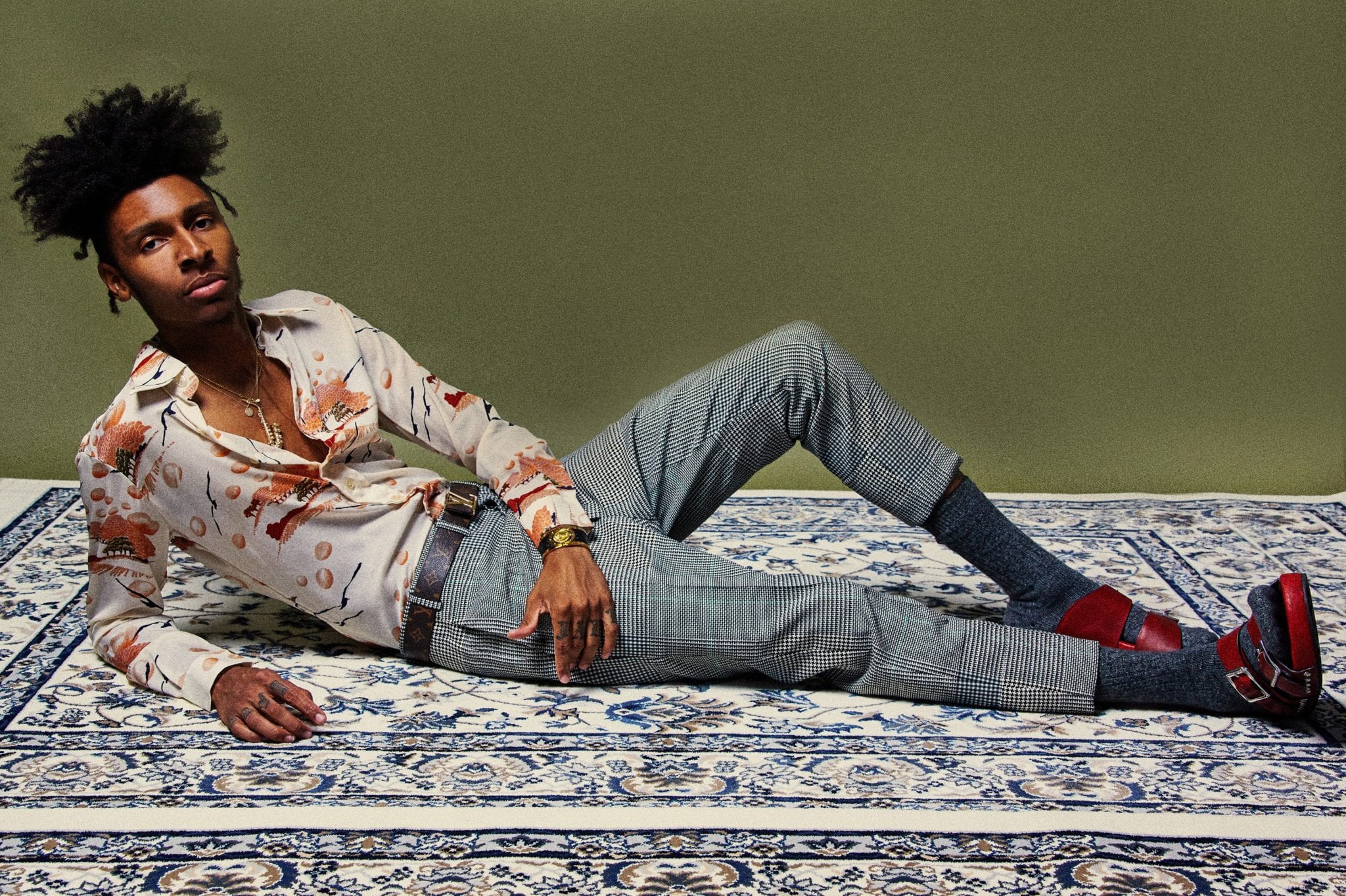Uncreative Music Artist Profile Masego African American man laying on a carpet with red sandals and colorful outfit