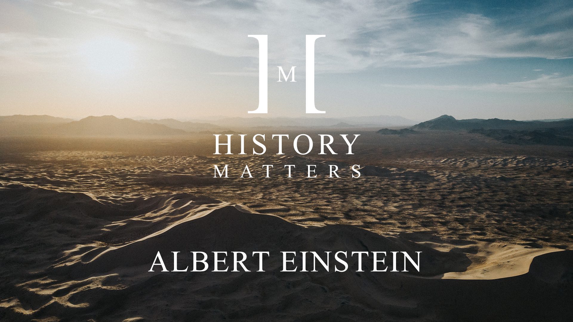 IU C&I Studios Page White HM Albert Einstein logo with background of sand dunes and mountains in a desert