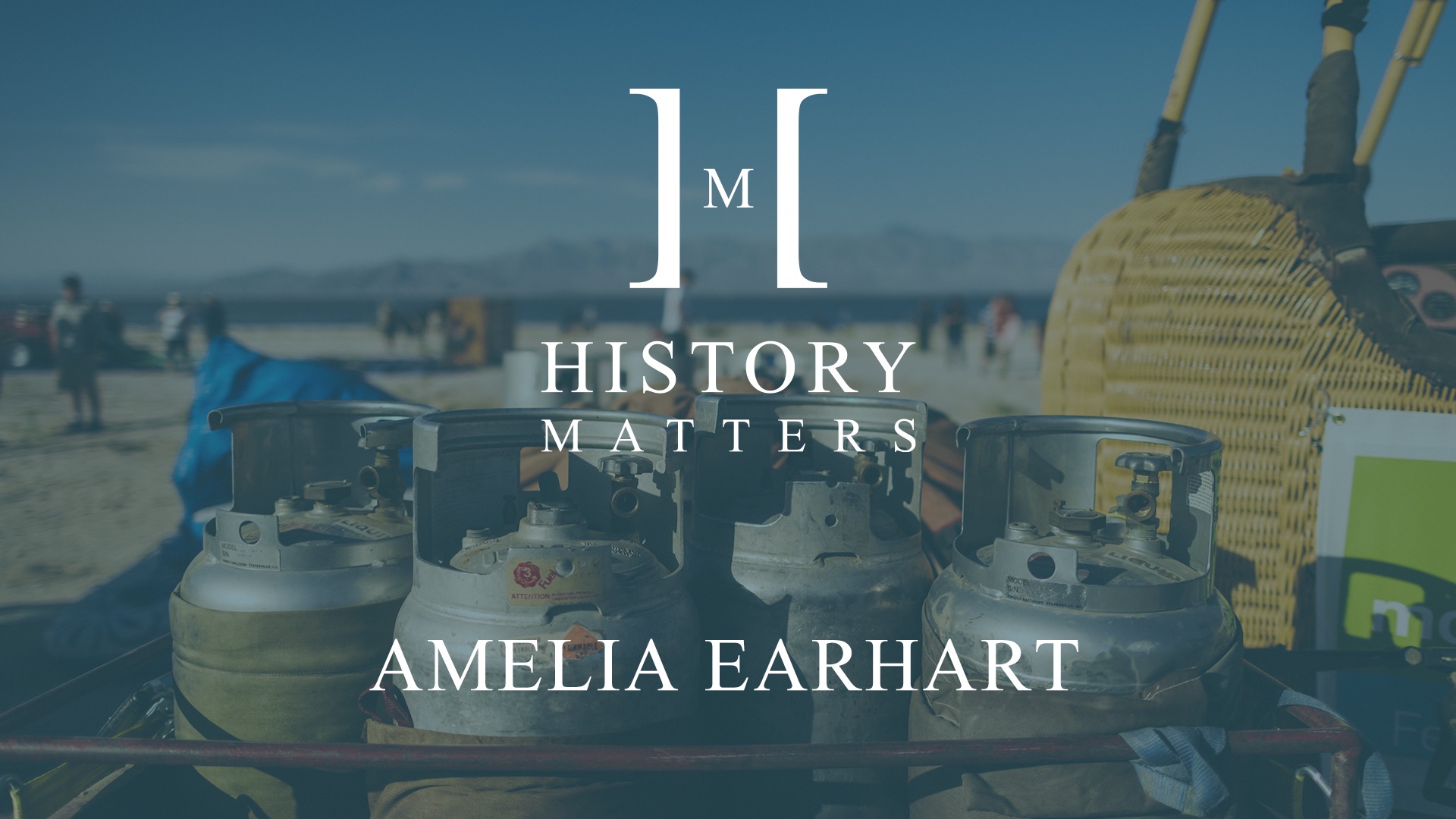 IU C&I Studios Page White HM Amelia Earhart logo with background of four fuel metal cannisters by a hot air balloon
