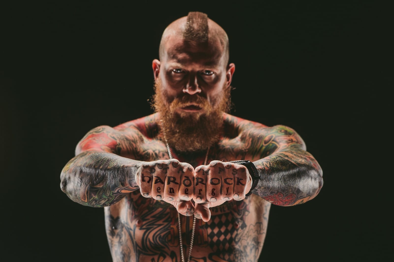 Tattooed man with mohawk posing with letters on his knuckles spelling out Hard Rock