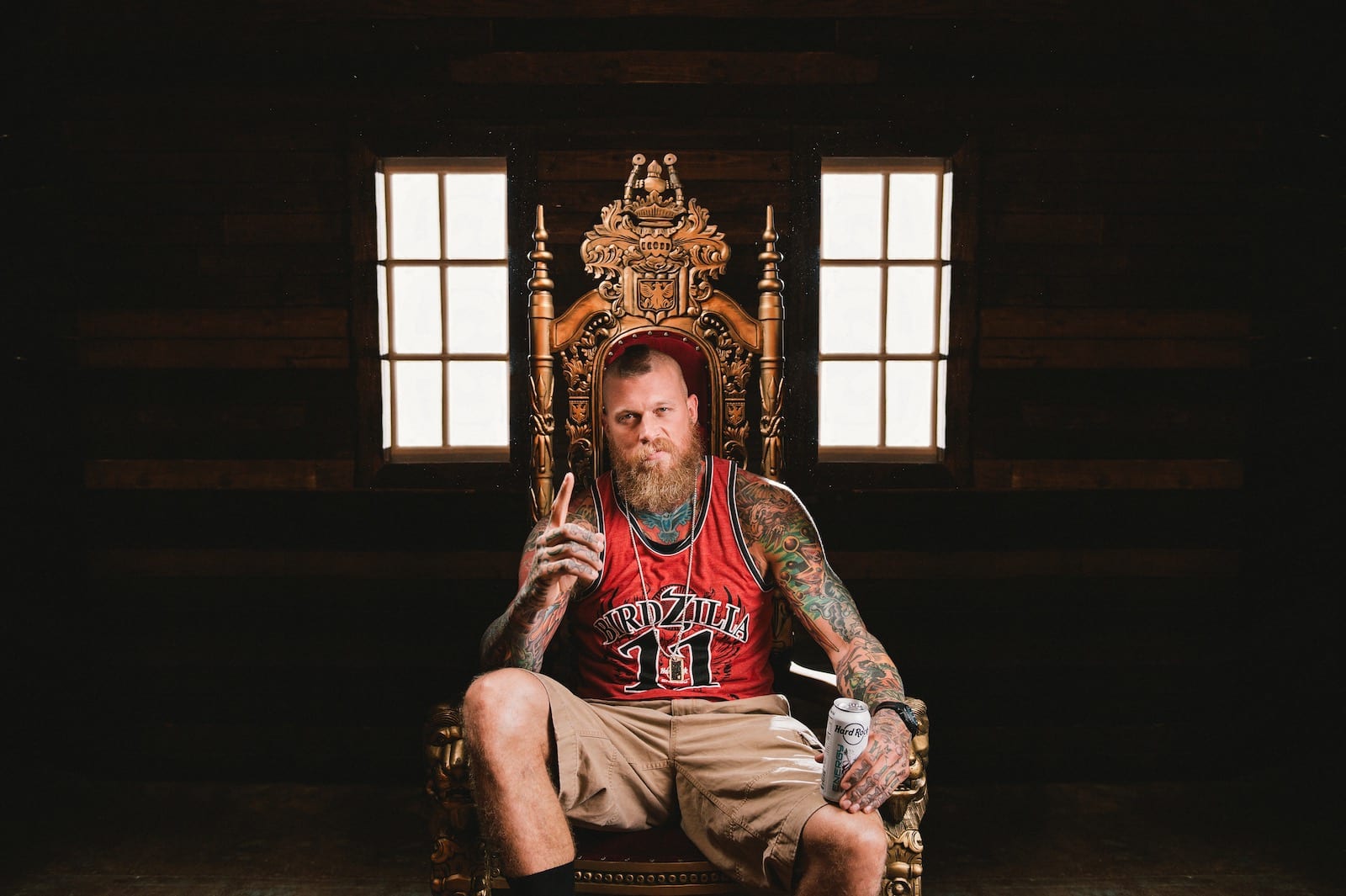 Bearded tattooed man sitting on a throne holding a Hard Rock Energy drink posing for camera