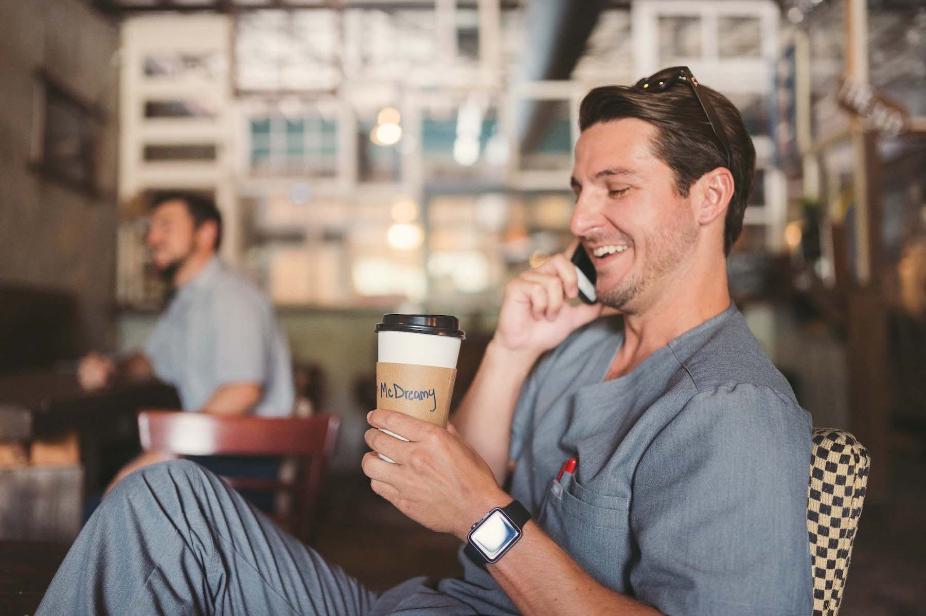 Brew Urban Cafe Man with short brown hair wearing a gray suit with sunglasses on his head holding a drink labelled McDreamy talking on a cellphone with another man in the background