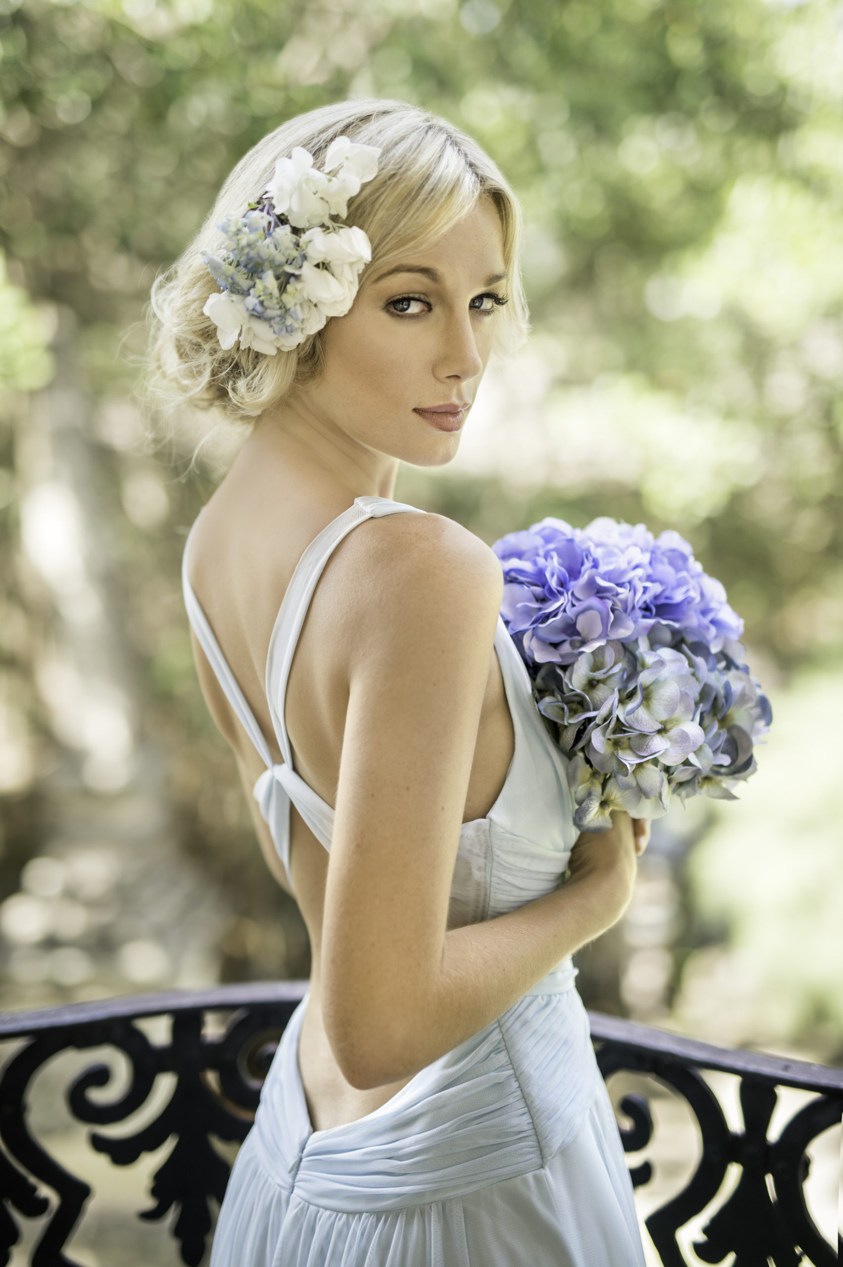 Woman with blond hair posing for camera looking over her shoulder holding a bouquet of flowers