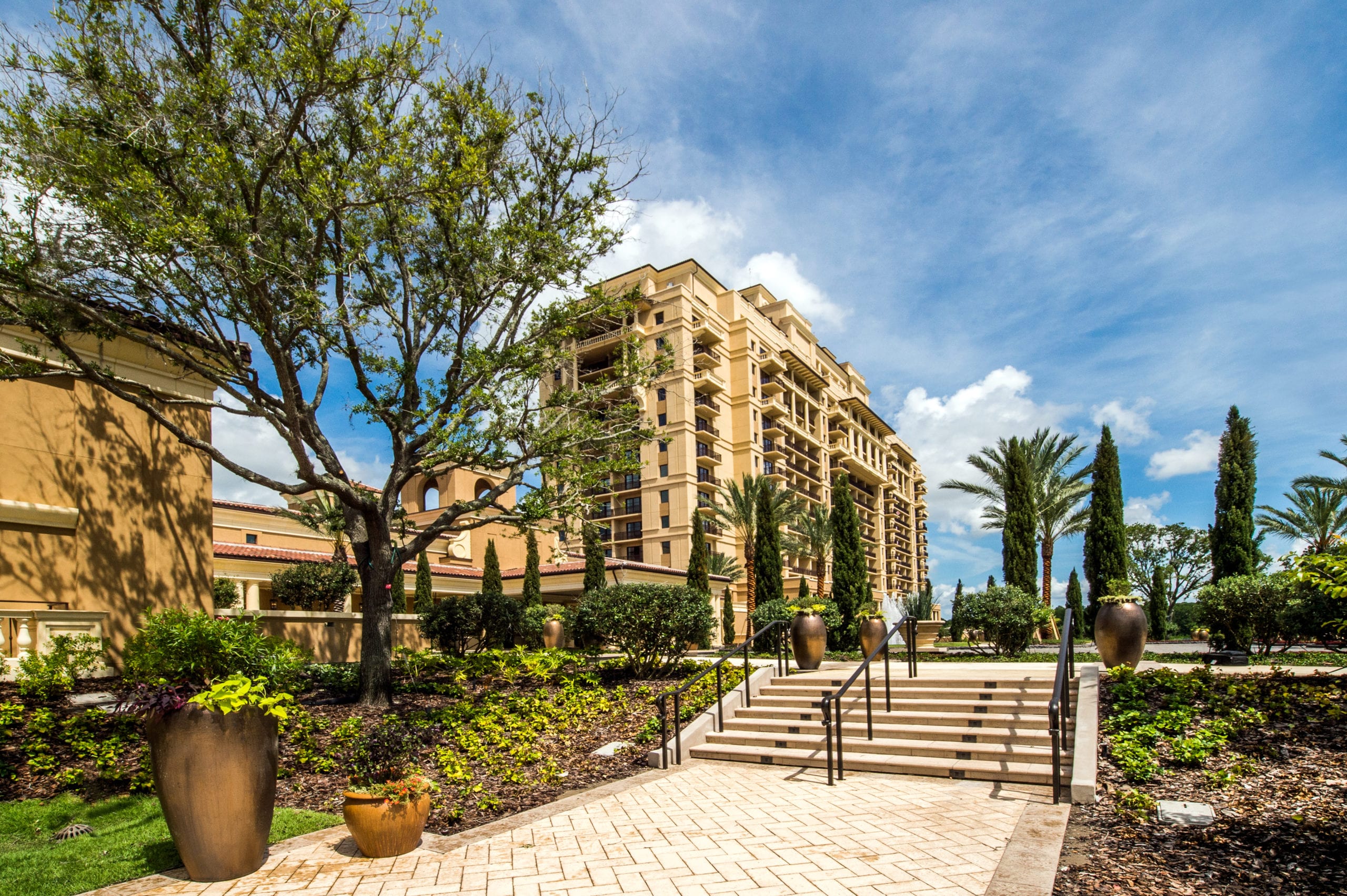Four Seasons Building by park with stairs with trees and palm trees under blue cloudy skies