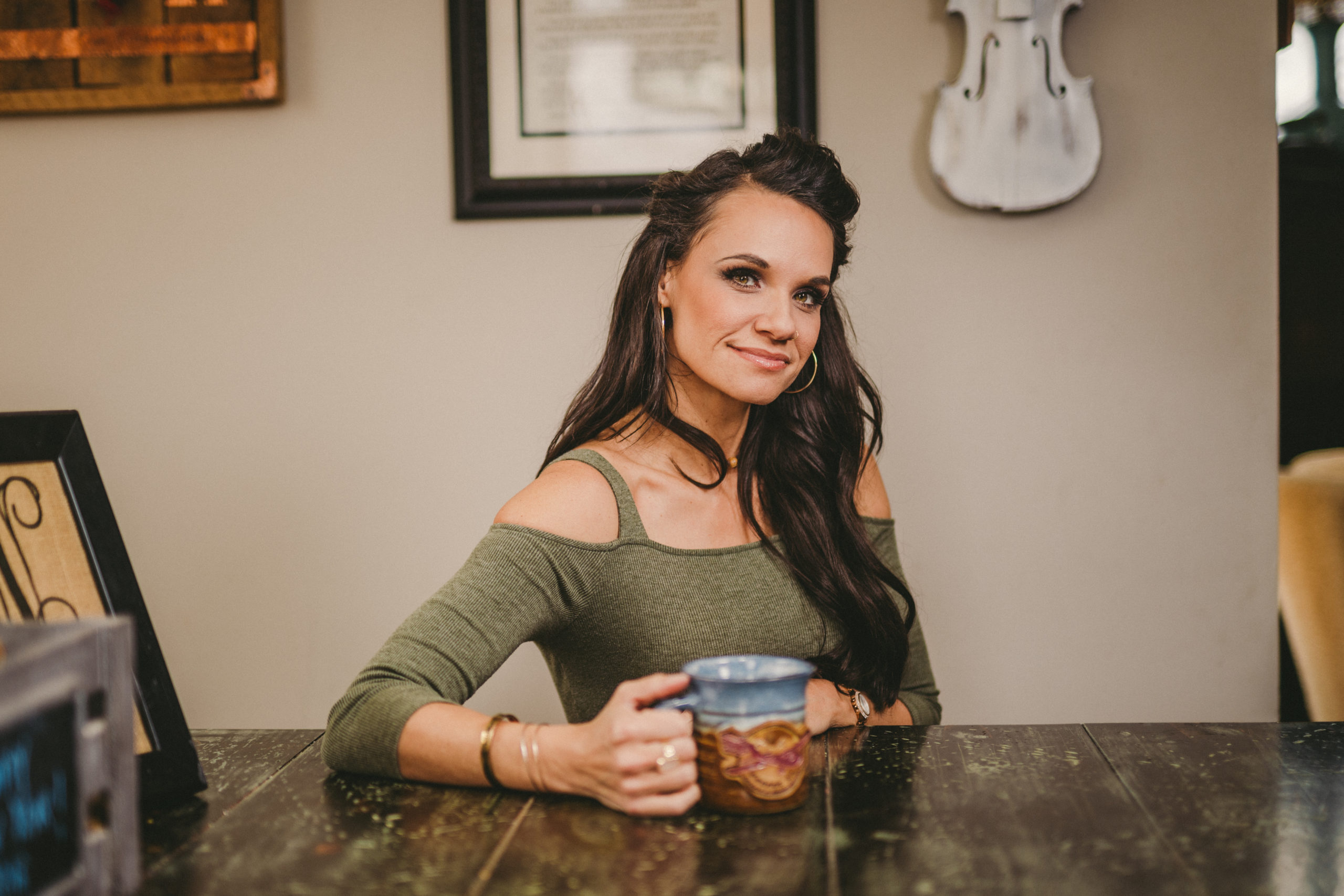 Woman with long brown hair posing for the camera holding a blue and brown coffee cup