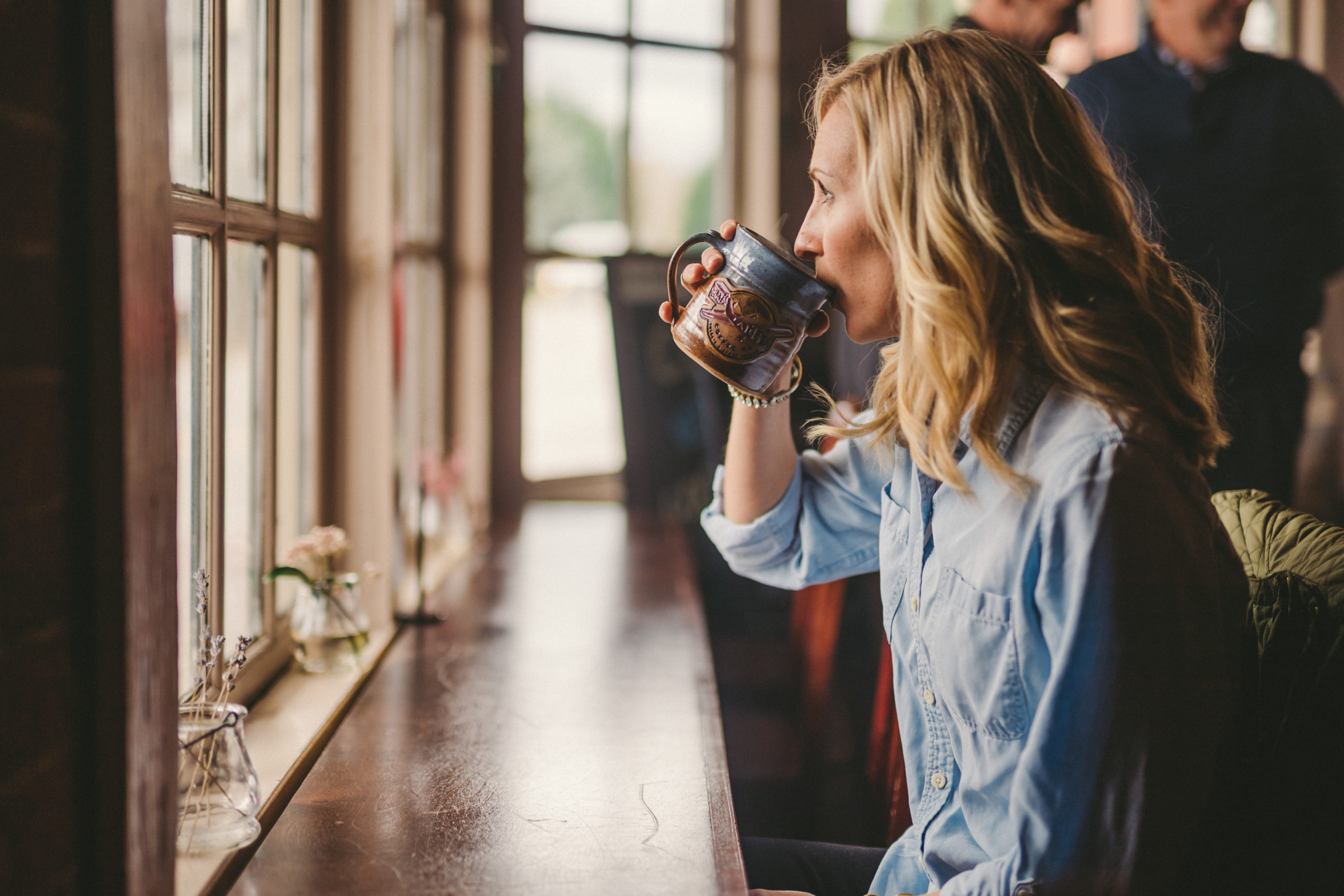 Side view of woman with long blond hair drinking coffee out of a blue and brown coffee cup