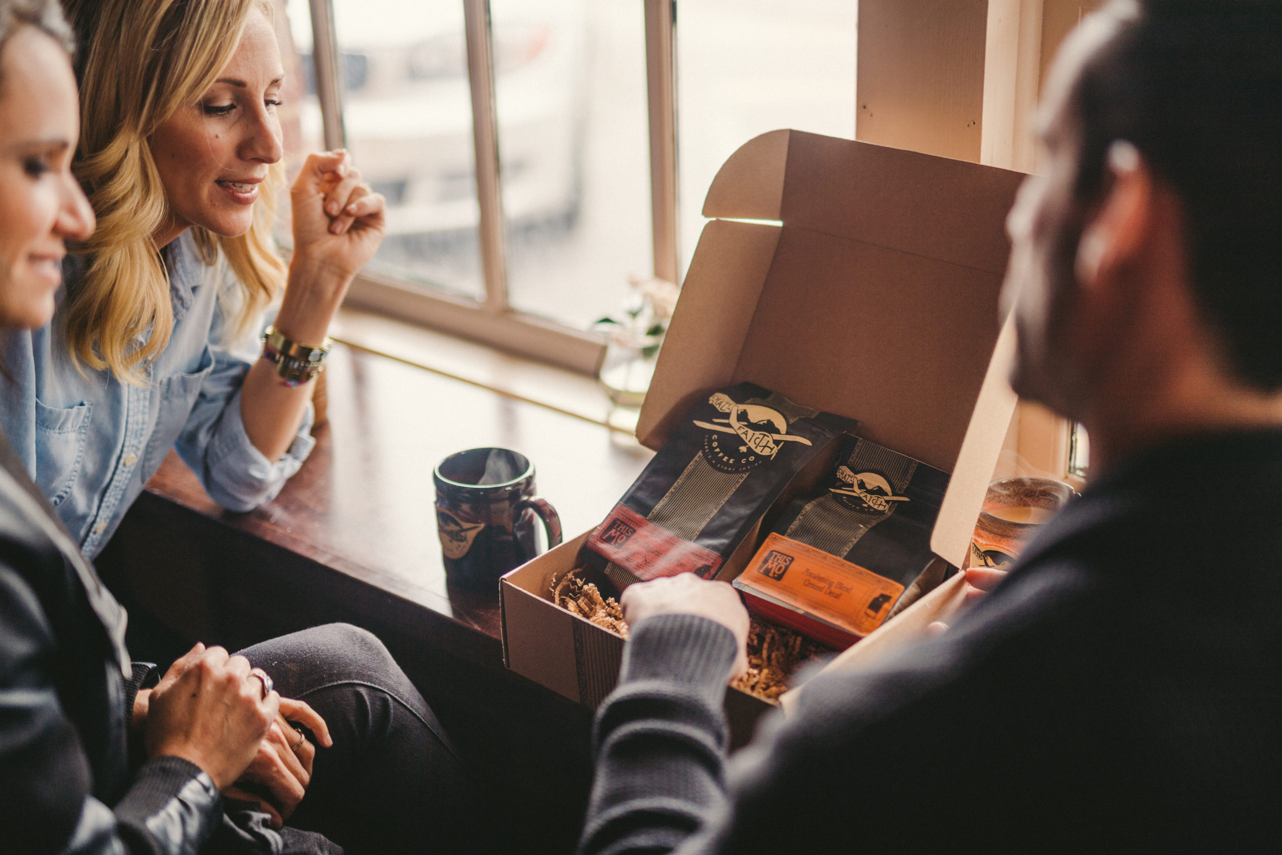 Two women and a man looking at box of Crazy Faith Coffee Co with a coffee cup next to it