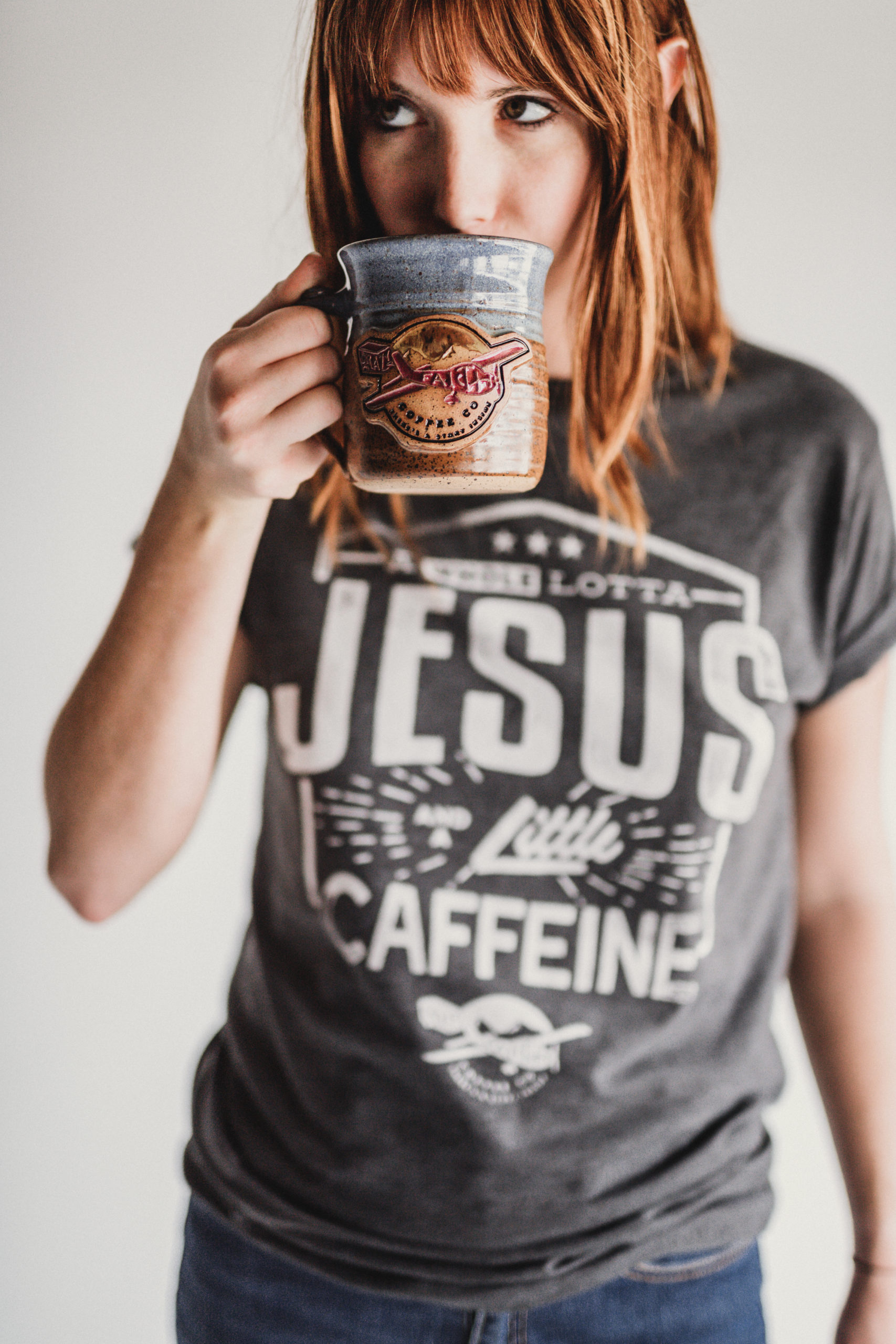 Woman wearing a gray t shirt that says A Whole Lotta Jesus and a Little Caffeine from Crazy Faith drinking some coffee from a gray coffee cup