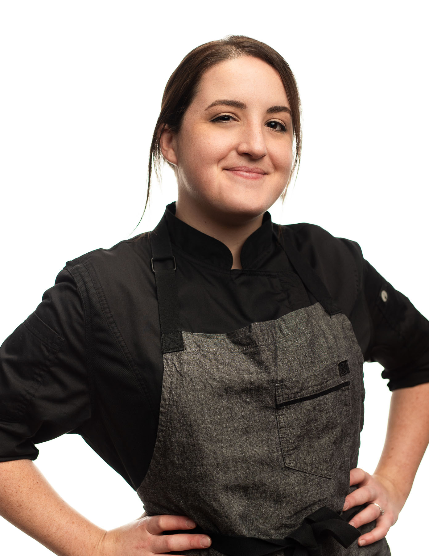Headshot of woman with short brown hair wearing a gray chef outfit smiling and posing for the camera