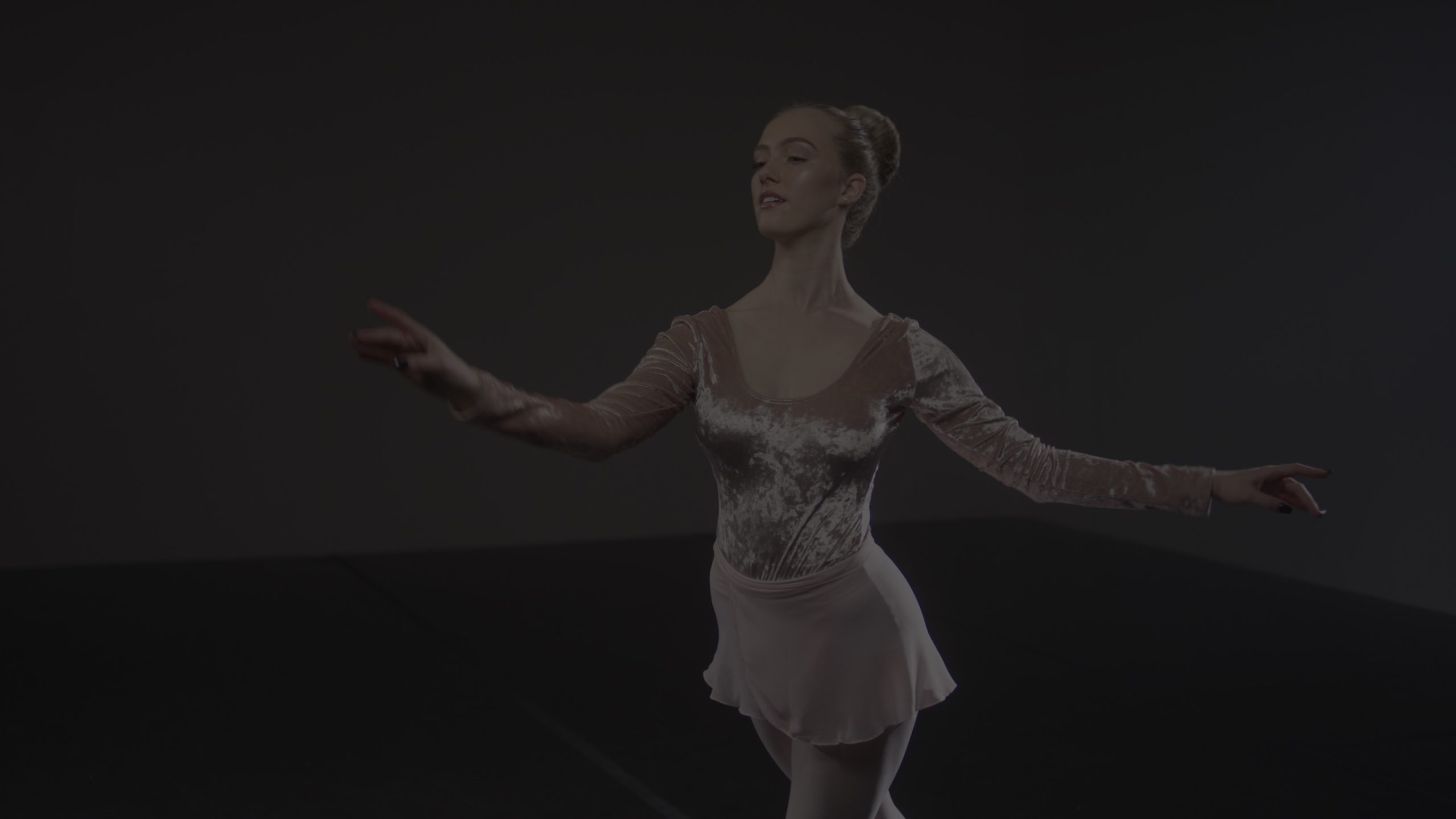 Video Production with Pretty Vulgar Dimmed image of a female dancer with short blond hair in a bun, long sleeved shirt and short dress skirt.