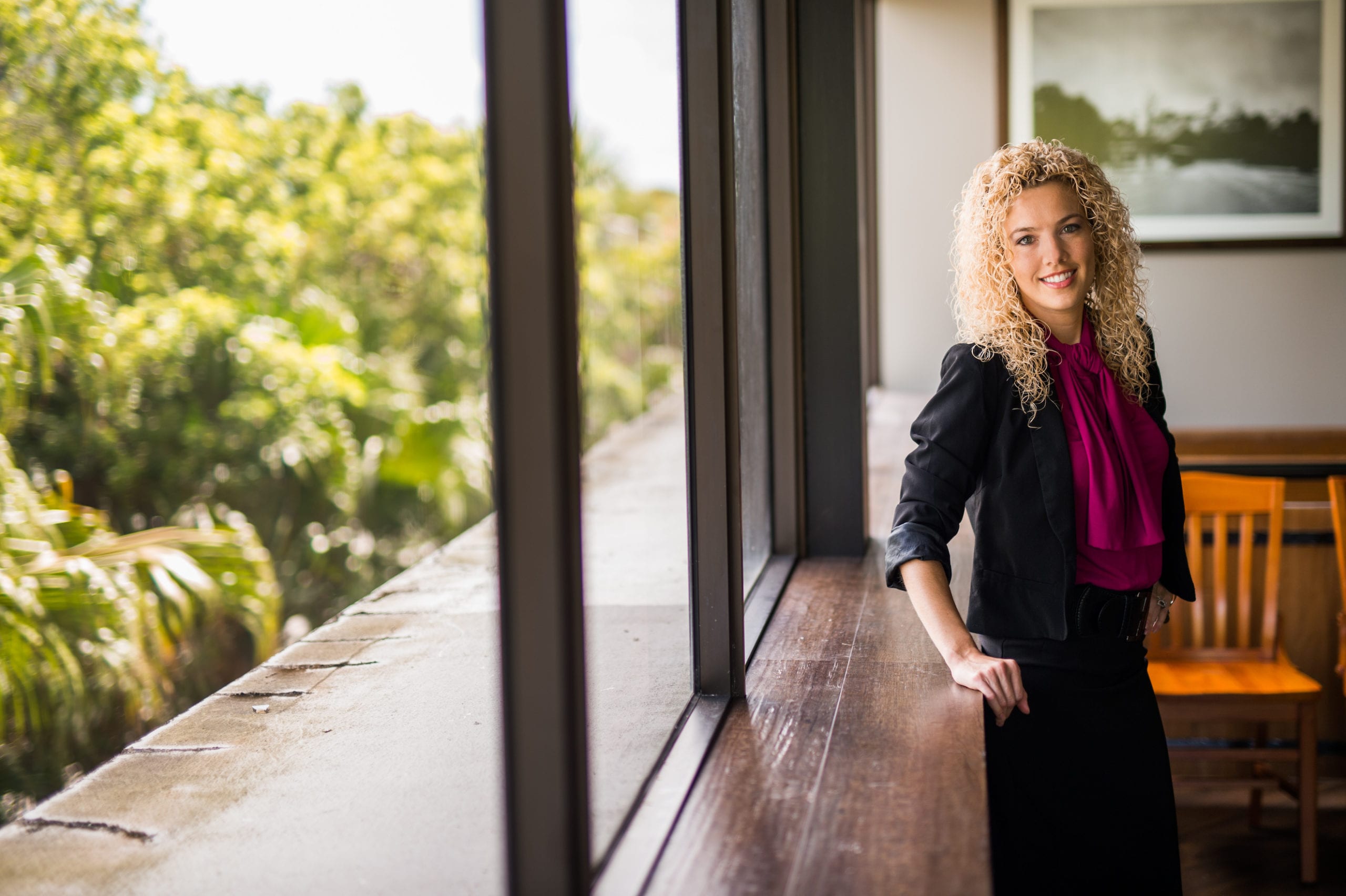 Kelley & Uustal Trial Attorneys Female attorney with curly blond hair leaning on a window sill smiling and posing for camera