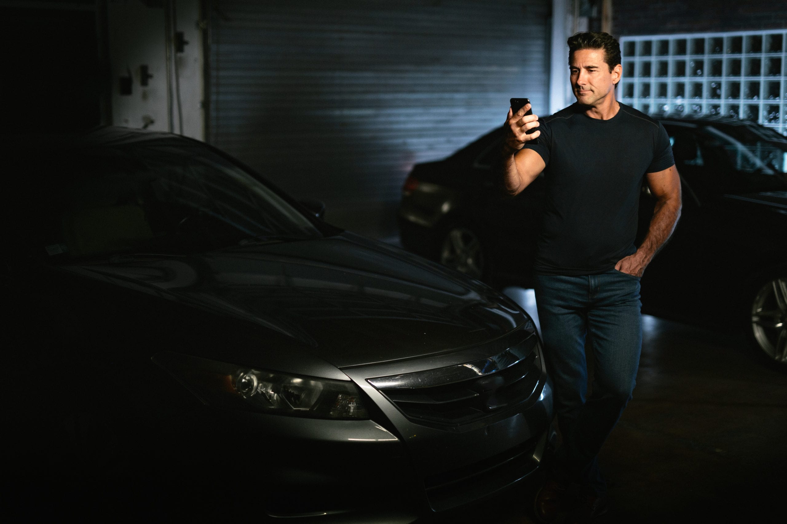 Young muscled man holding a cell phone standing between two black cars
