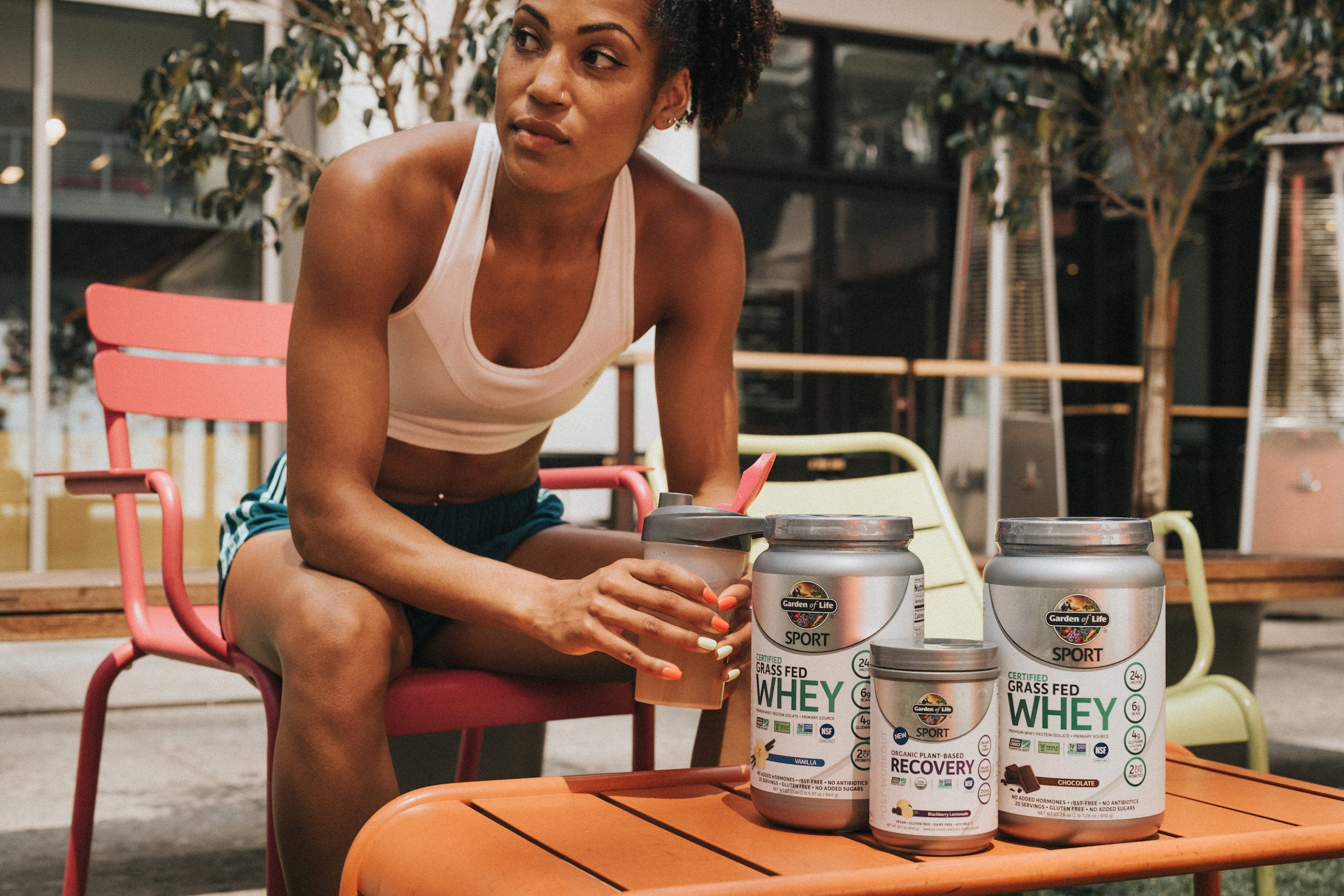 Karelle Edwards sitting on a pink chair looking off camera by an orange table with Garden of Life Whey and plant based recovery powders