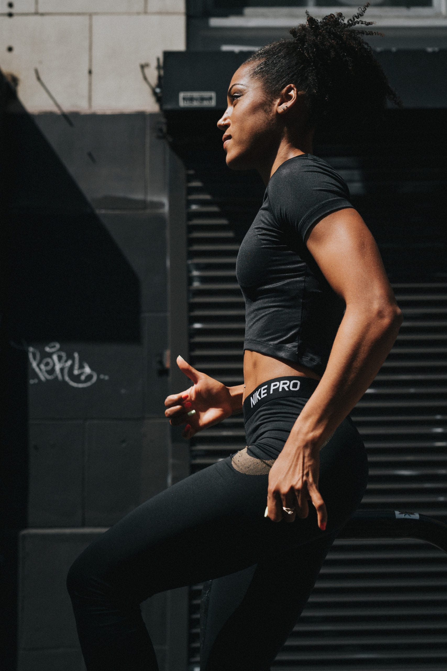 Side profile of Karelle Edwards doing leg stretches by a black building