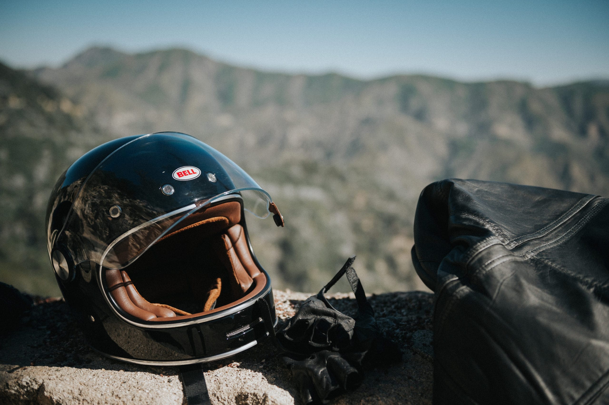 Bell helmet sitting on a rock next to black leather biker gloves and black leather jacket