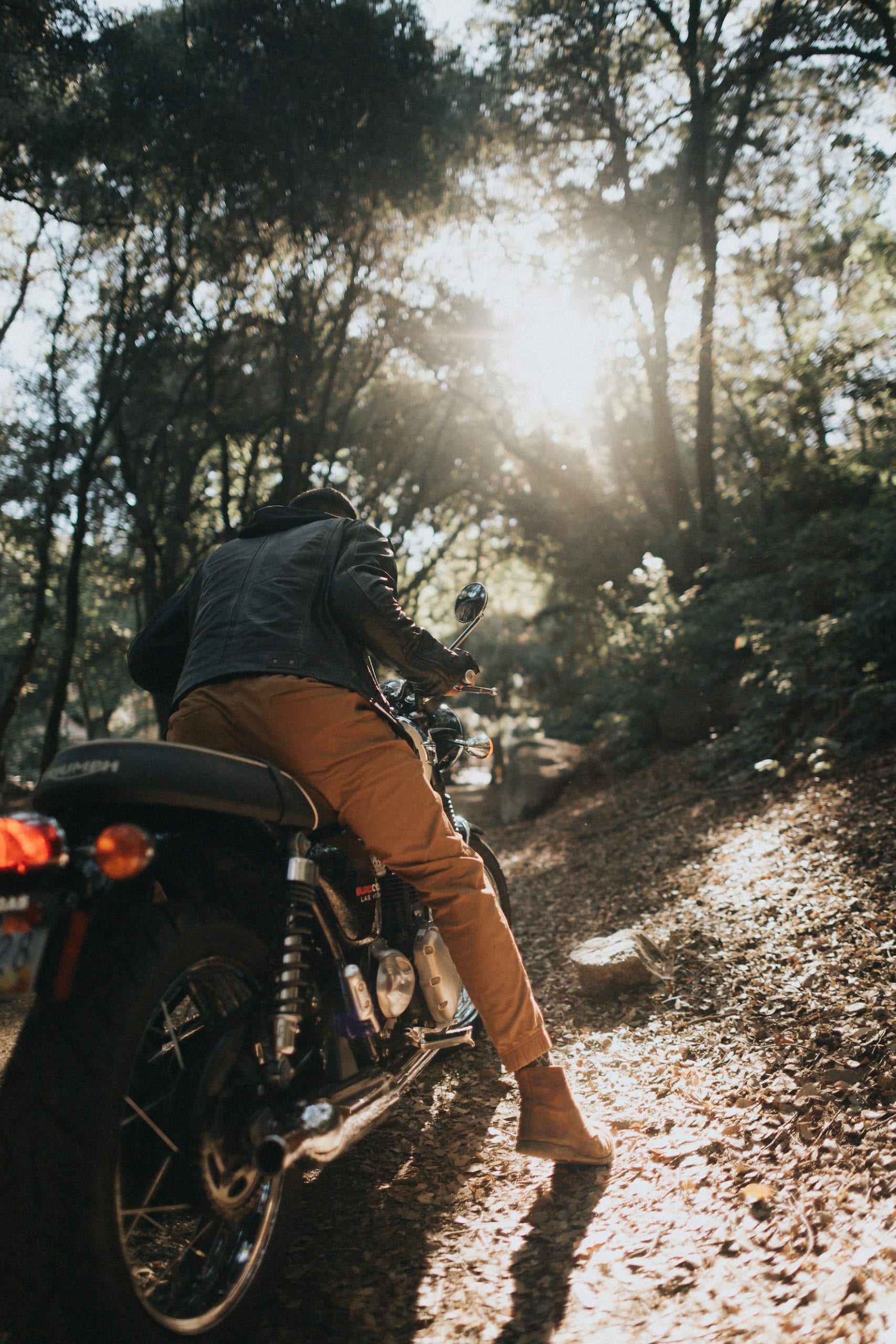 View from behind of motorcycle rider sitting on the motorcycle going up a forest path