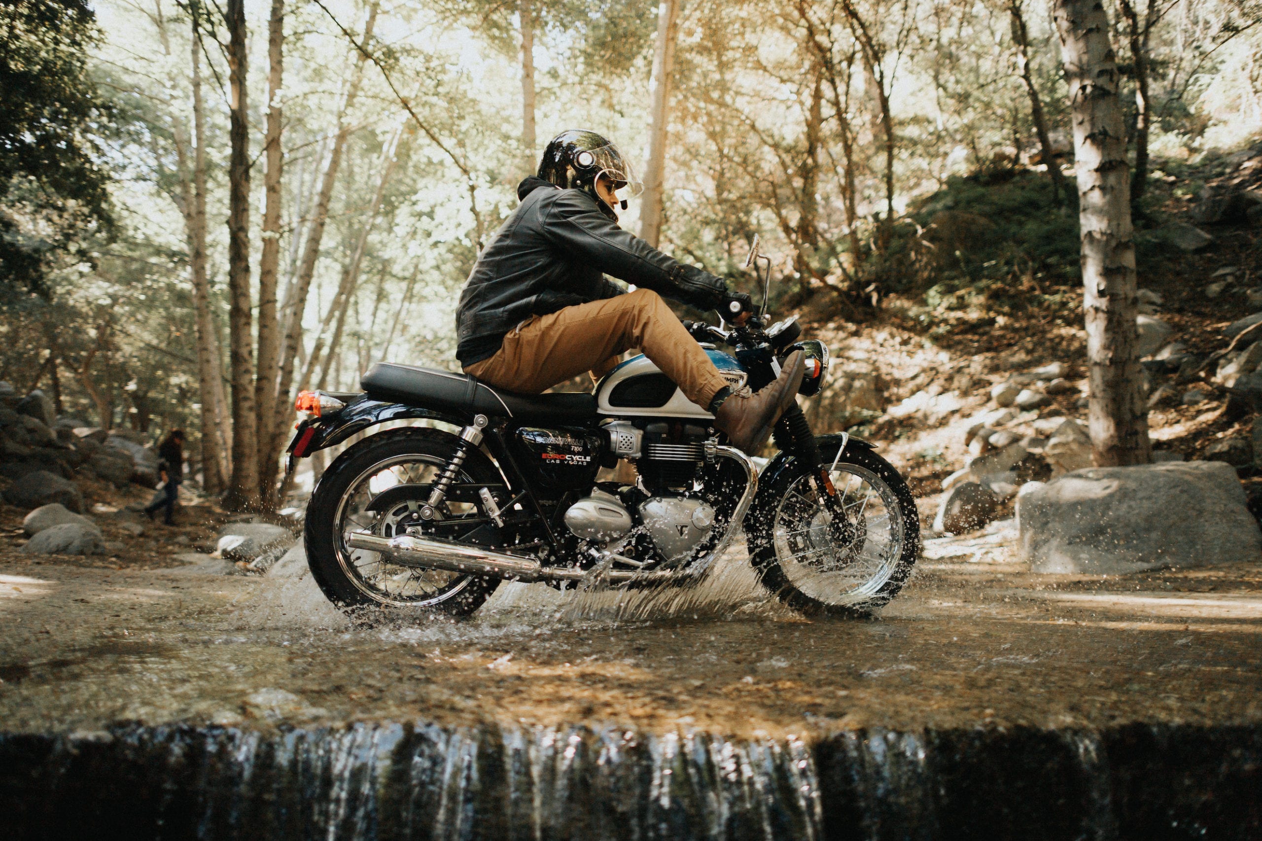 Motorcycle rider riding through a shallow creek in Angeles National Forest with feet in the air