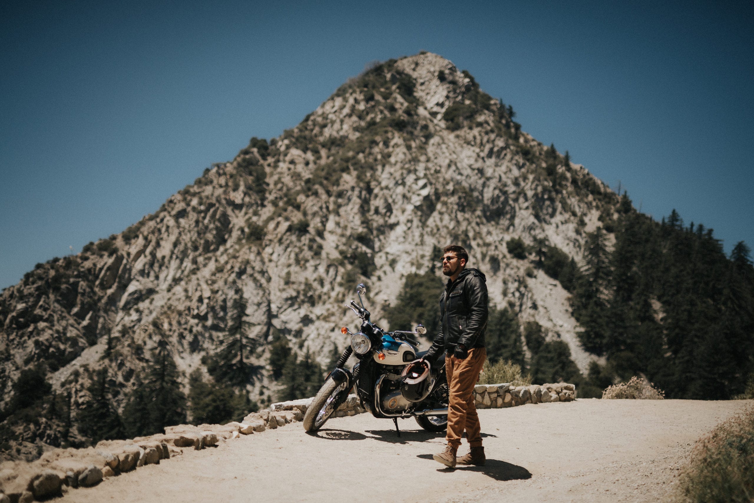 Motorcycle rider standing in front of a Bonneville T100 motorcycle with mountain peak in the backdrop