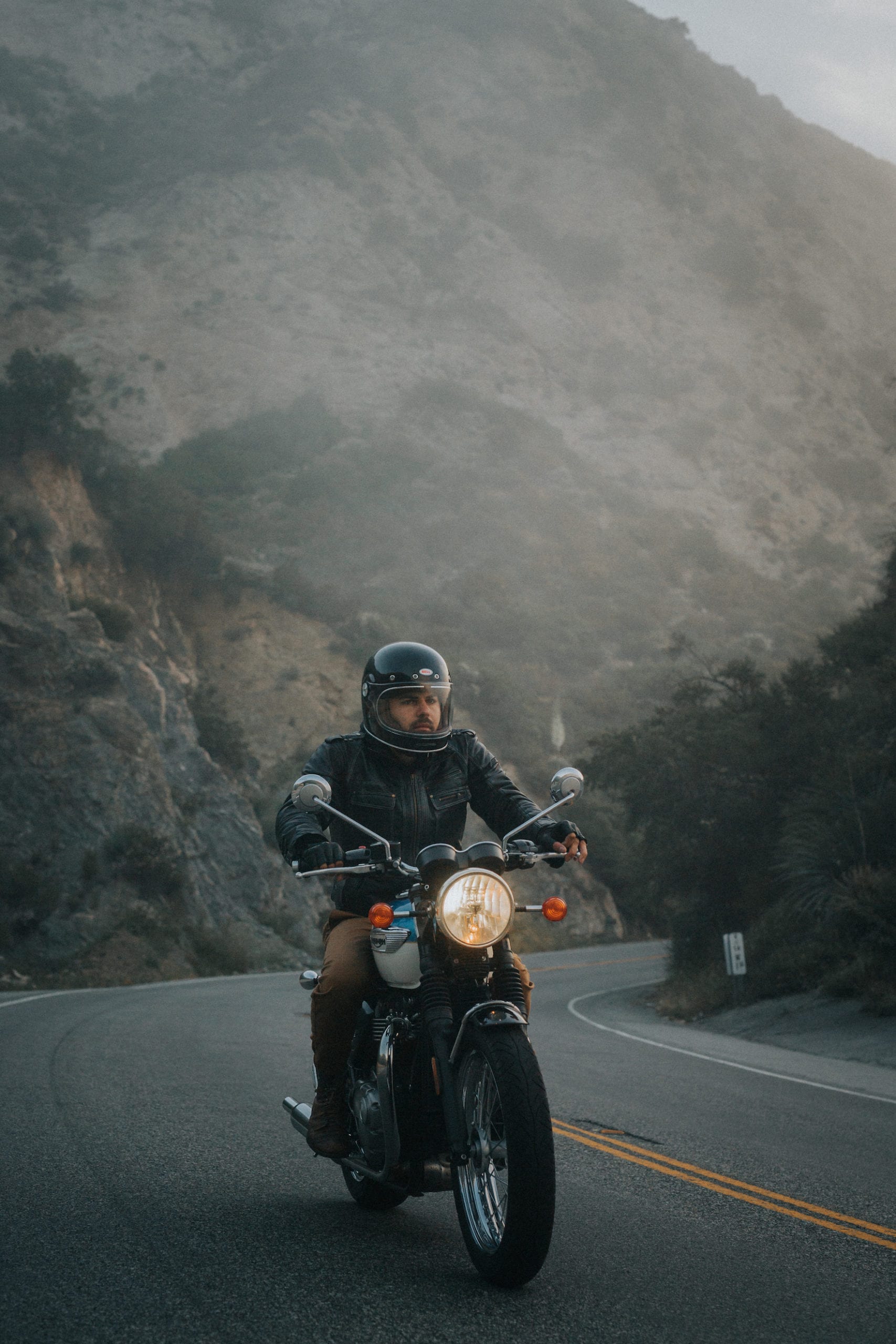 Motorcycle rider wearing a helmet and motorcycle gear riding up the mountain on a hazy morning.