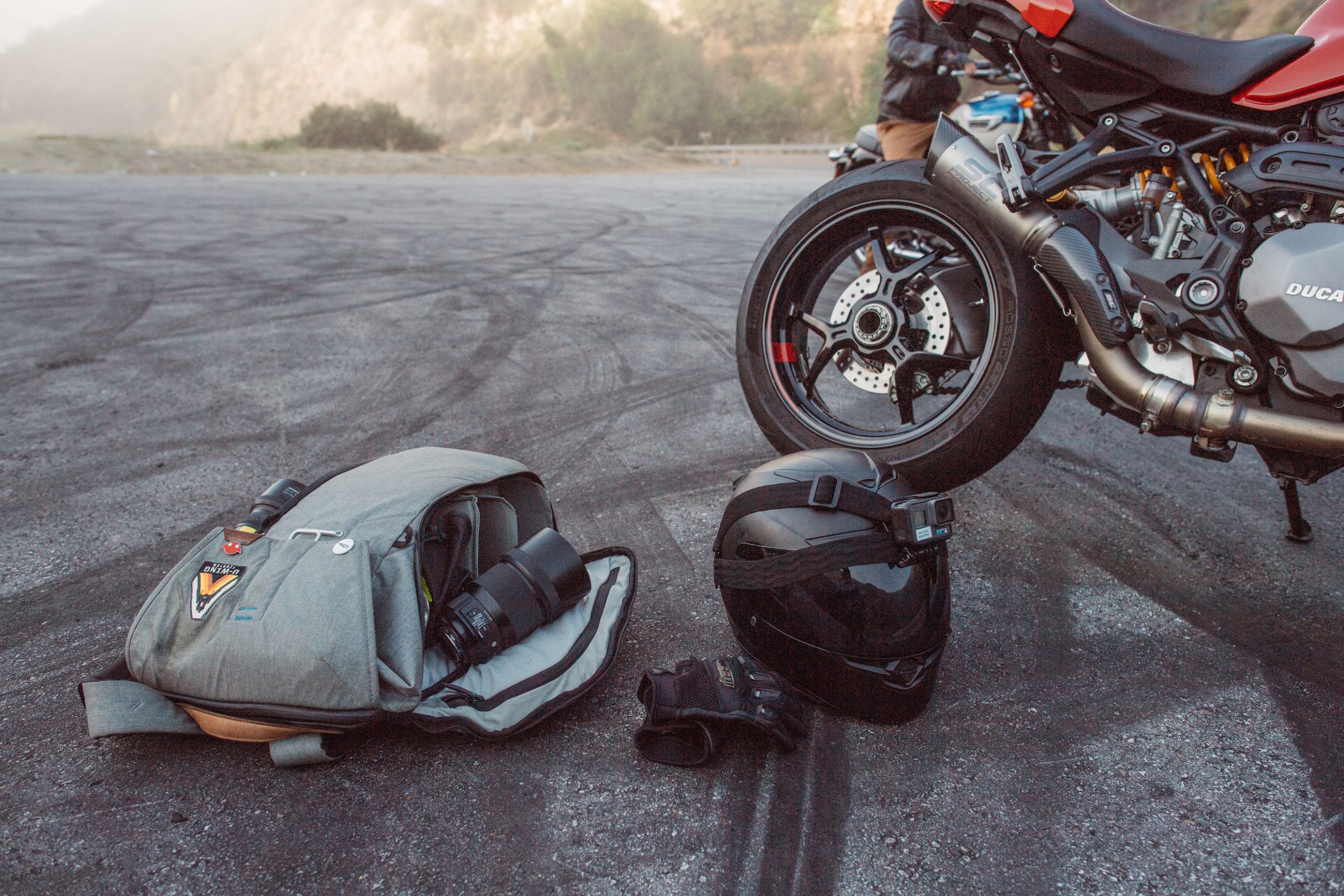 View of the back side of the bike along with helmet with camera, backpack and leather gloves on the ground