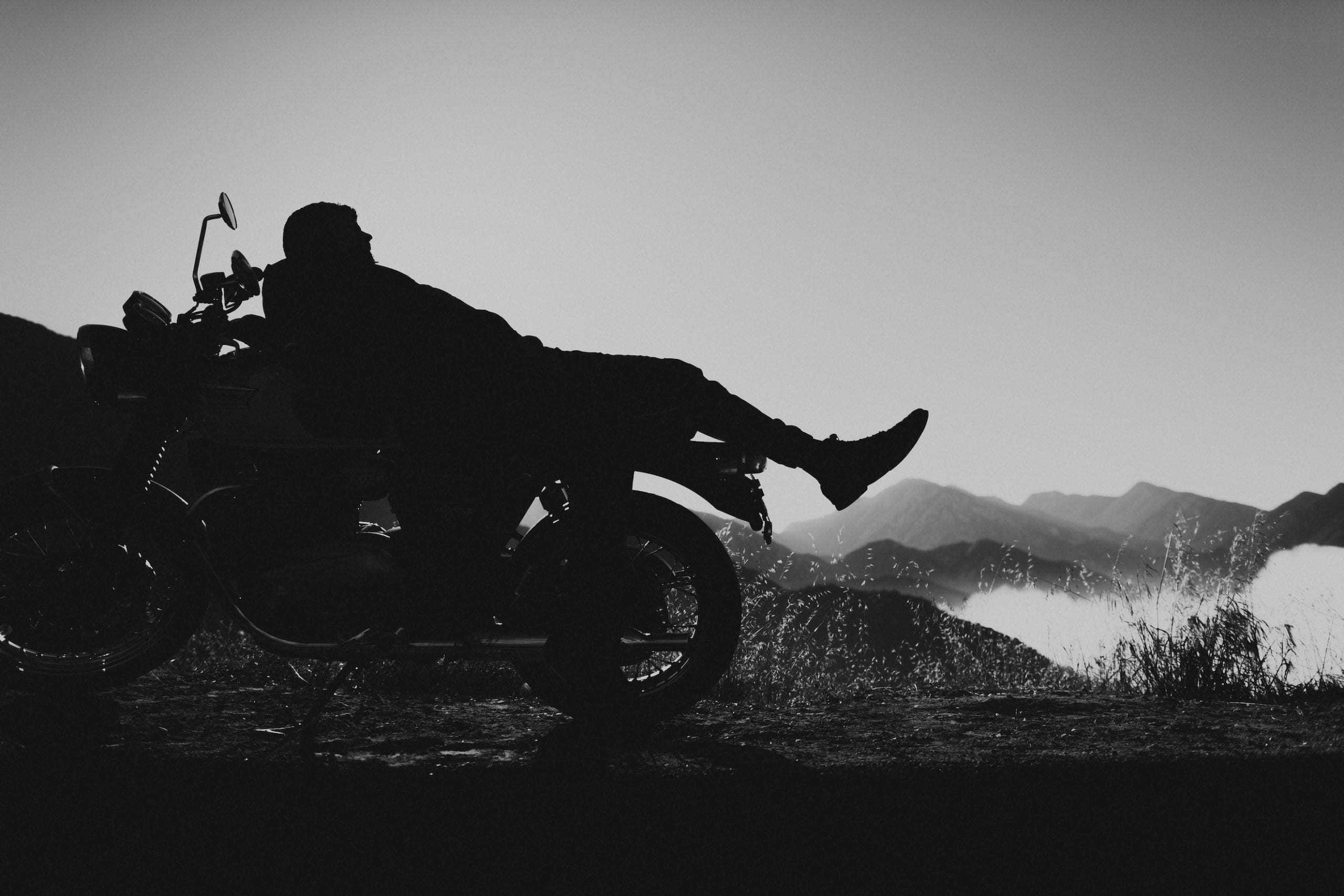 The motorcycle rider relaxes laying on the back of the motorcycle posing for the camera
