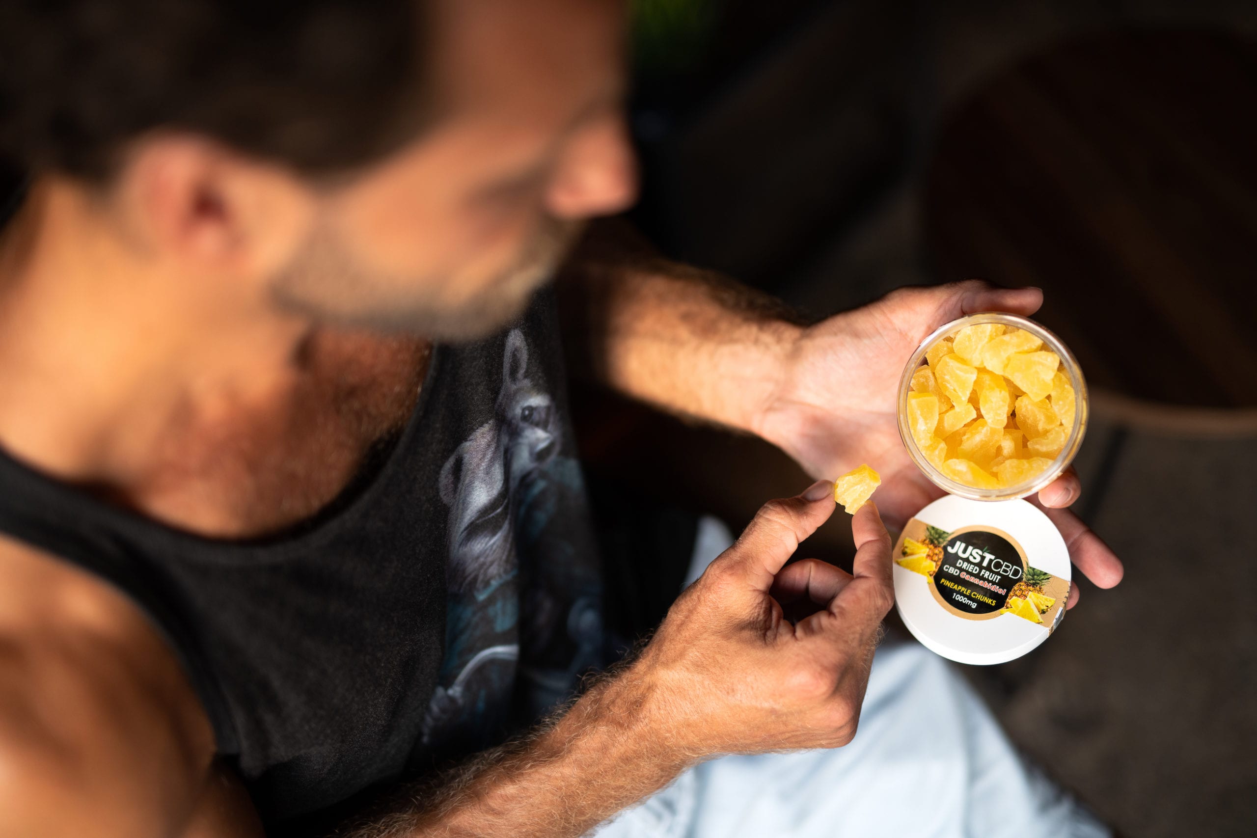 Overhead view of a man taking a pineapple chunk from JUSTCPD dried fruit container