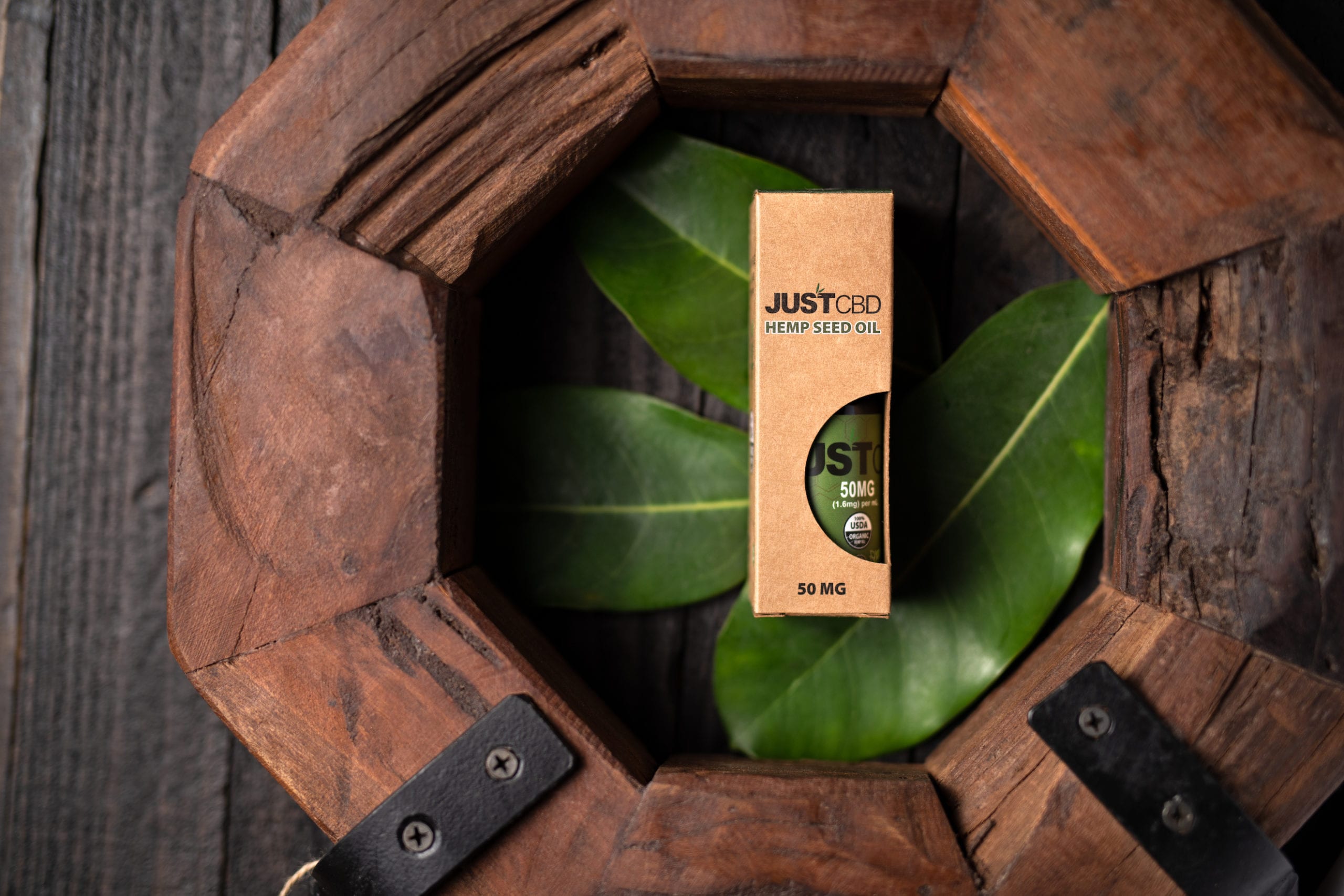 JustCBD Hemp Seed Oil package on display on green plant leaves surrounded by wood blocks