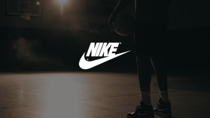 IU C&I Studios Page Nike Sneakers Conceptual Advertisement White Nike Logo With A Background Showing The Lower Half Of An African American Man Poised Holding A Basketball On A Basketball Court With A Light Shining On Him In Semi Darkness
