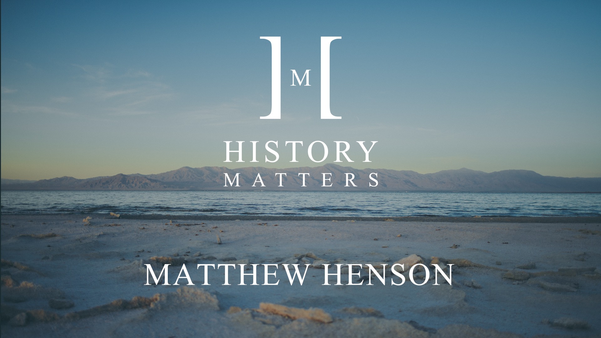 IU C&I Studios Page White HM Matthew Henson logo with background view of sand and beach with mountains in the background