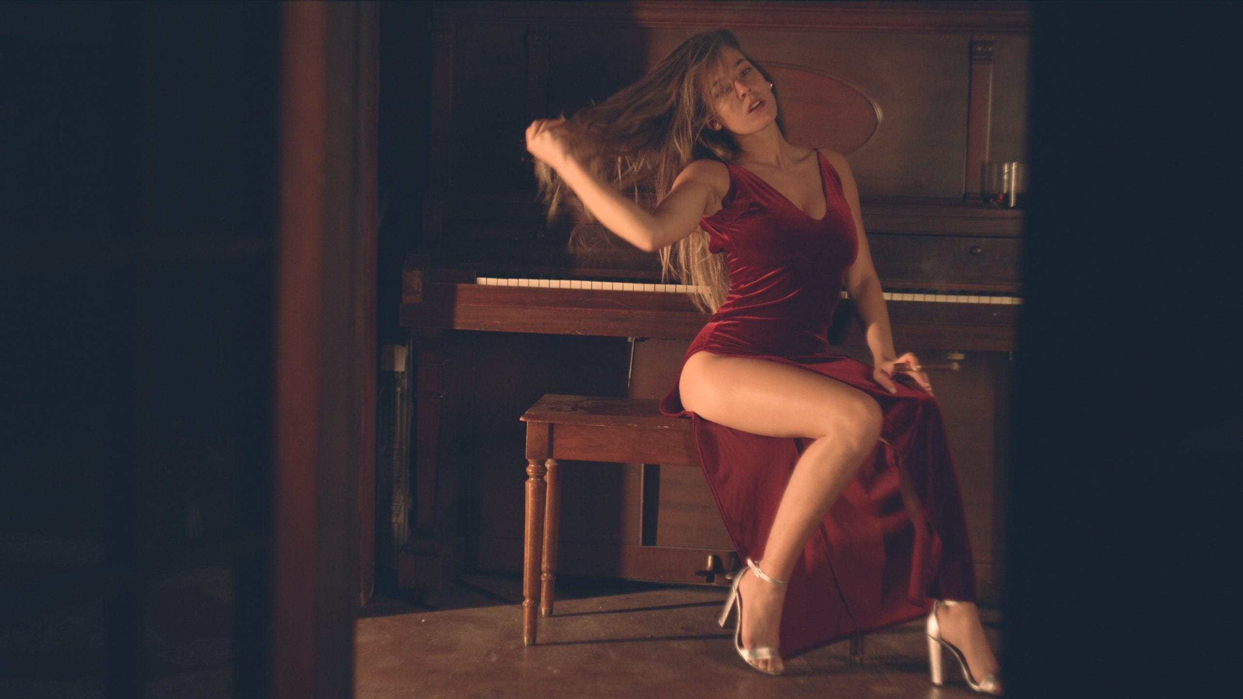 Sabela Model posing for camera sitting at a piano wearing a red dress and high heels holding a cigar