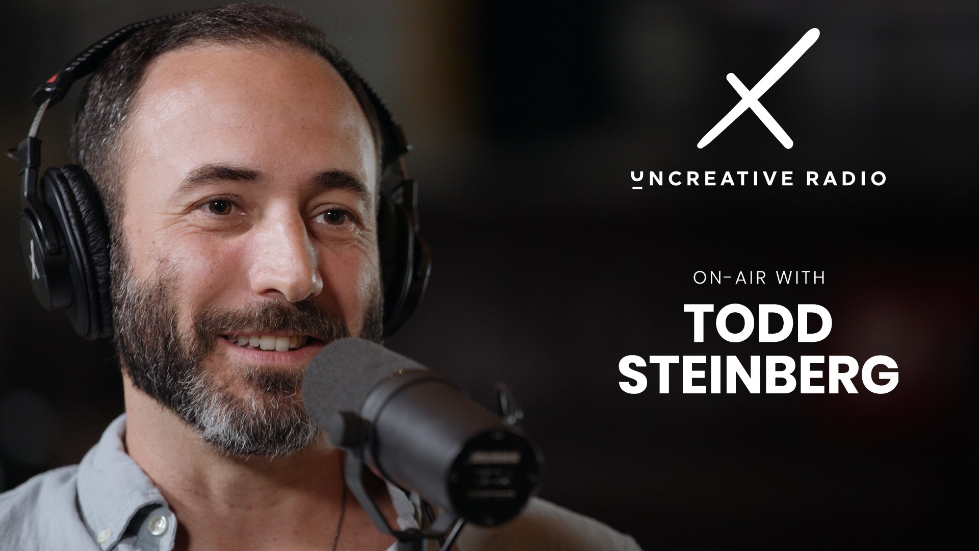 Uncreative Radio on air with Todd Steinberg with short hair and beard wearing black headphones talking into a microphone