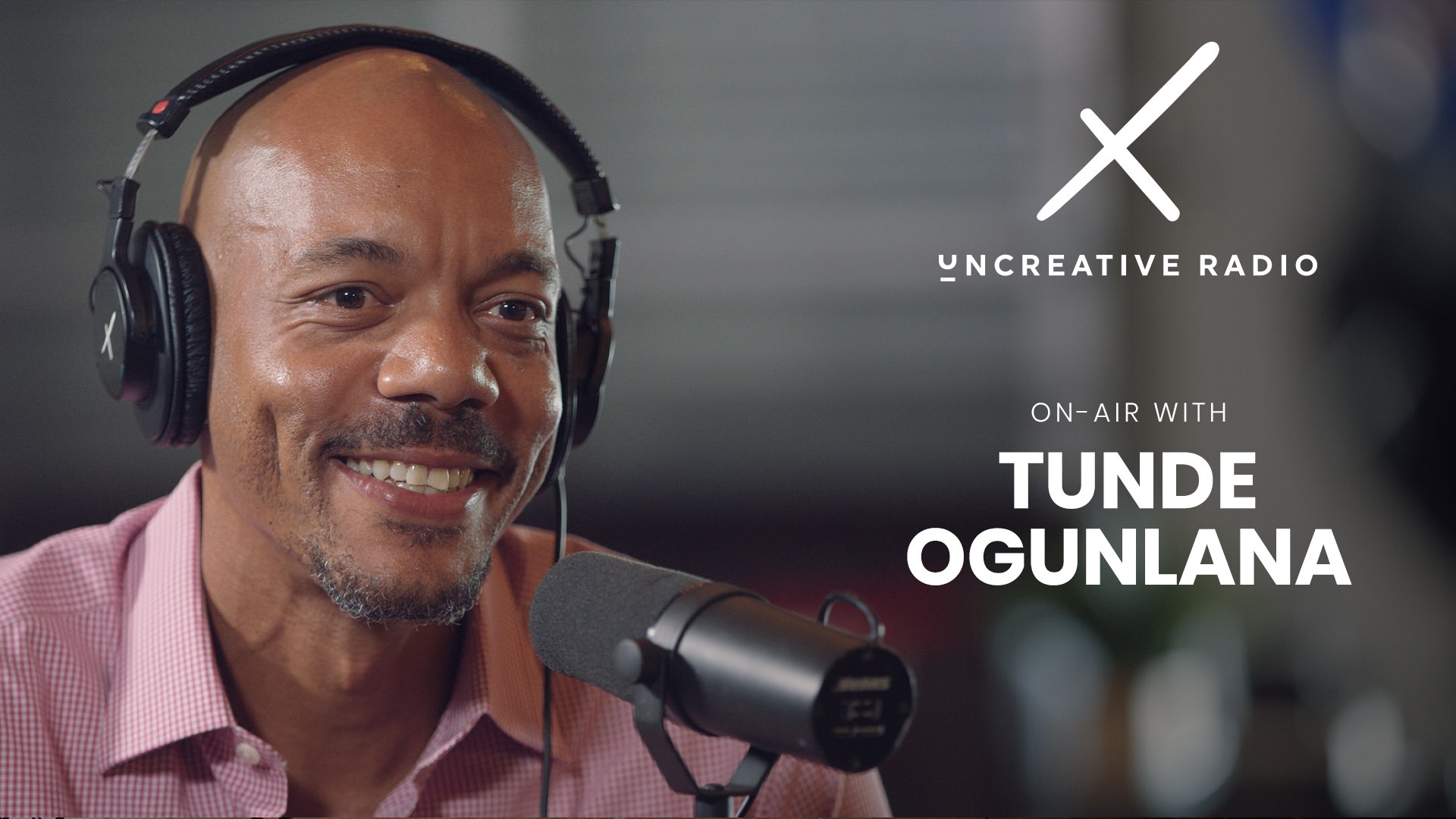 Uncreative Radio on air with Tunde Ogunlana with him wearing red and white checkered shirt and black headphones smiling by microphone