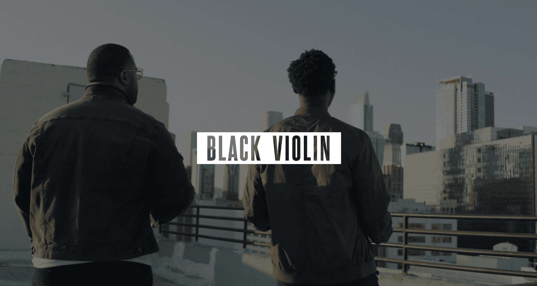 Video Production Services to Podcast Recording Studio Gray Black Violin logo on white against a dimmed background of two men standing on a concrete rooftop looking out over the city
