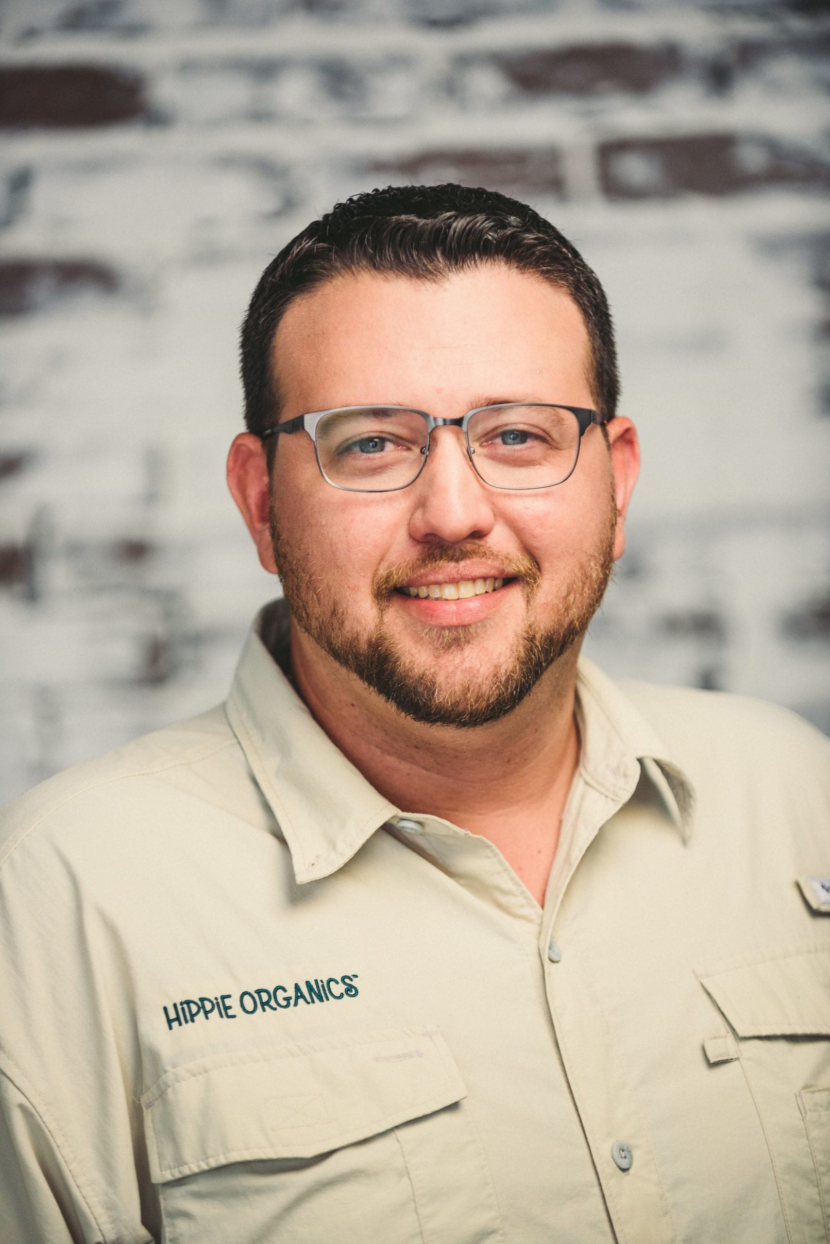 Headshot of male Hippee Organics employee with short hair and beard wearing glasses wearing beige uniform