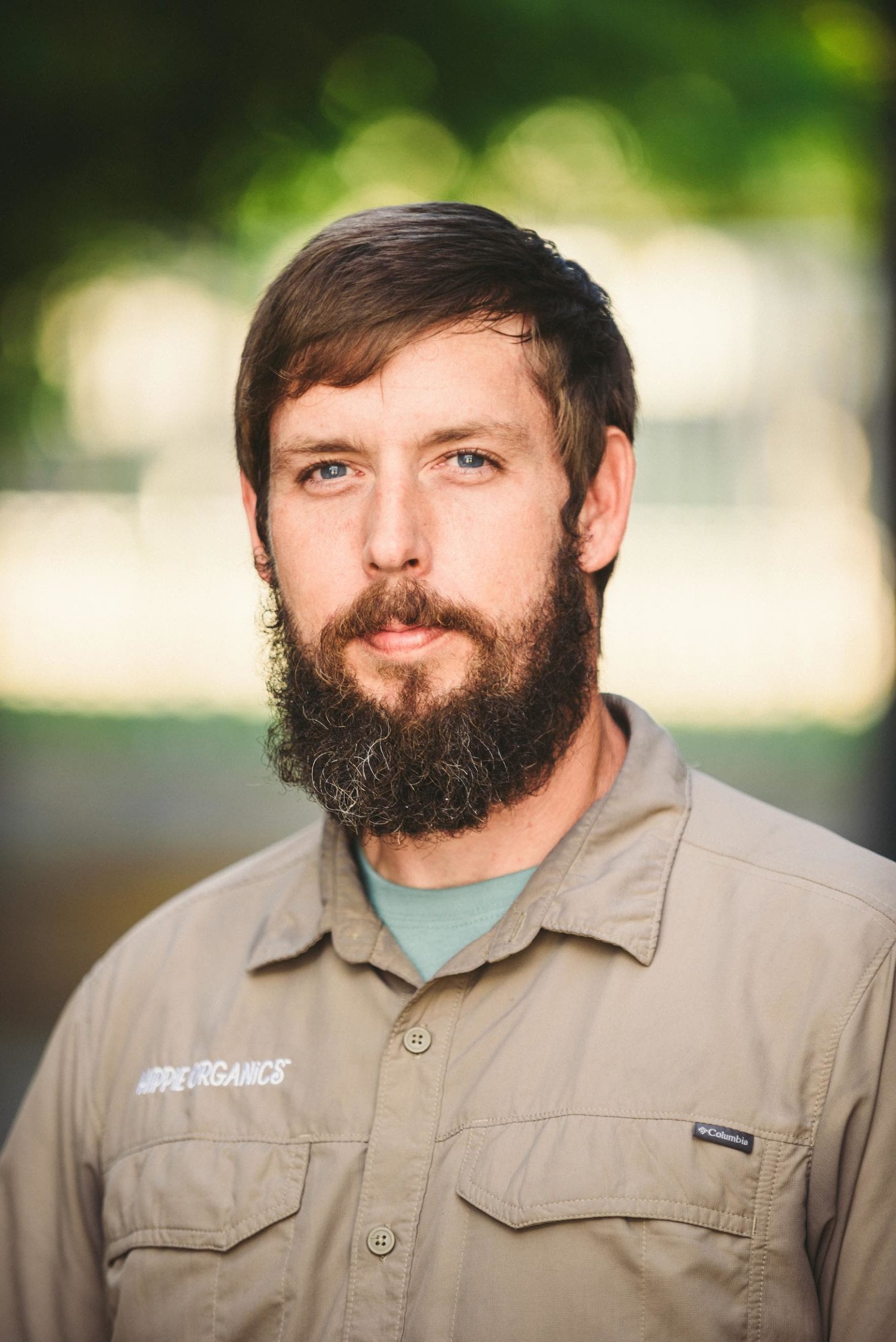 Headshot of male Hippee Organics employee with brown short hair and beard wearing beige uniform