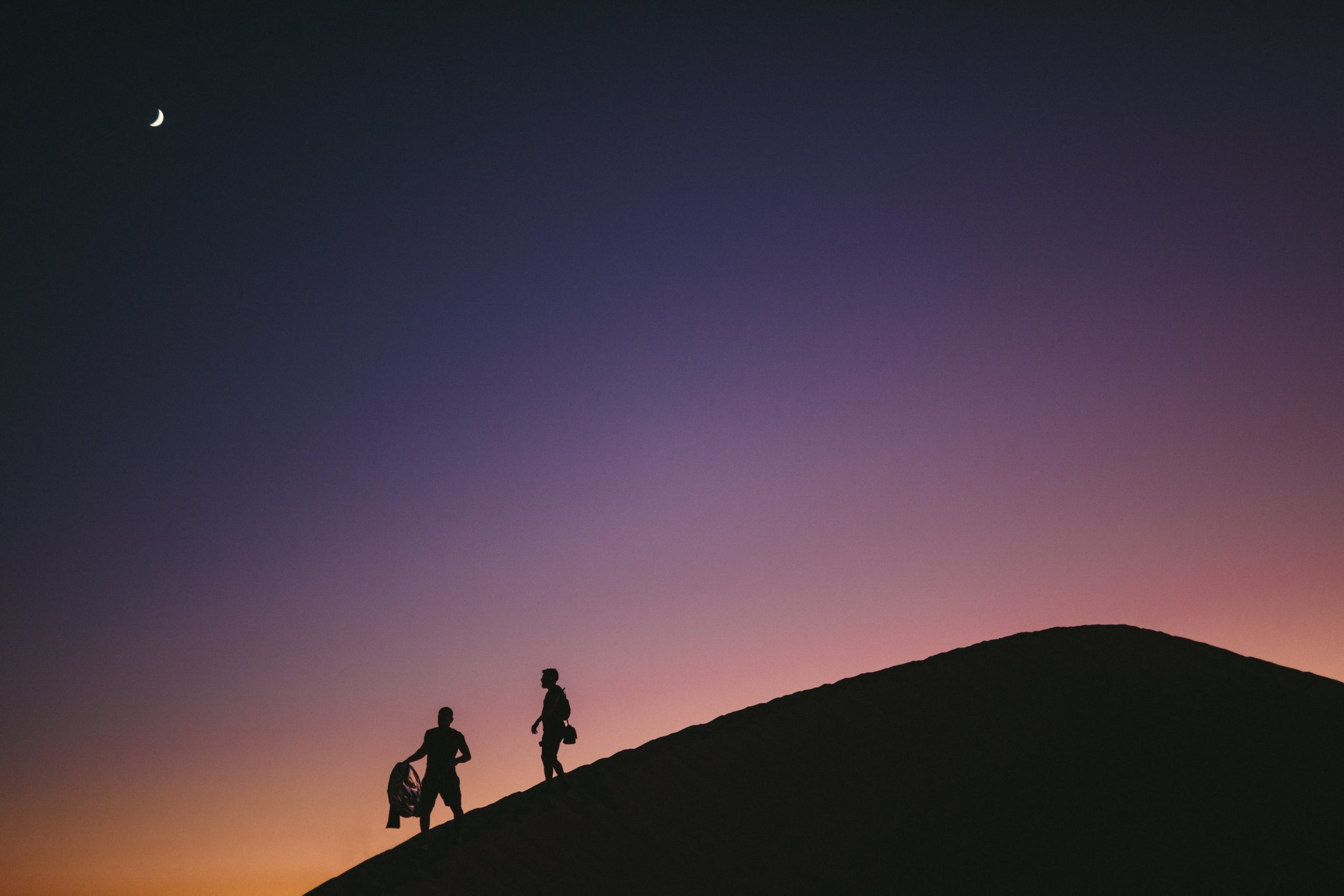 Two crew members at dusk walking down a sand cliff