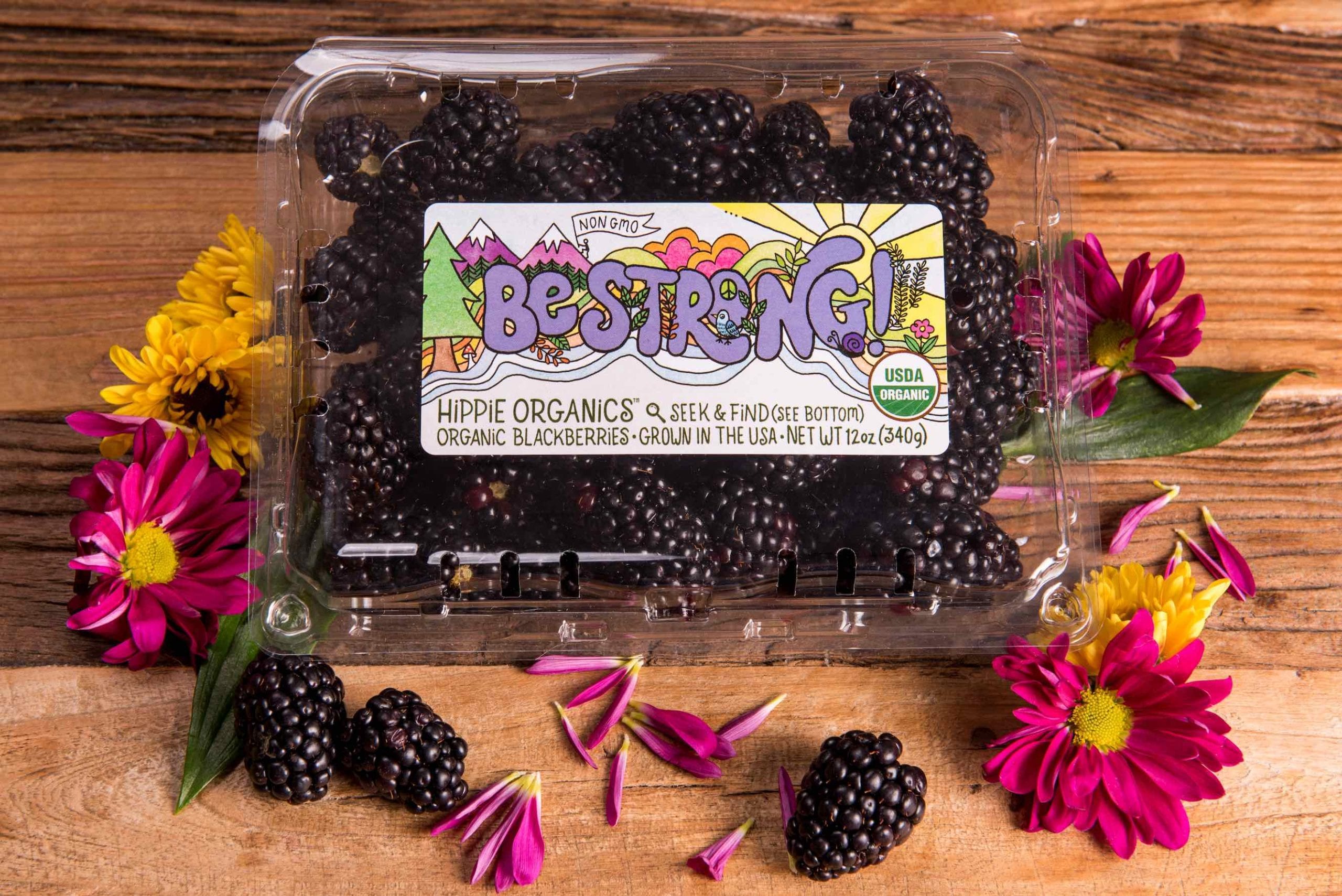 Aerial closeup view of package of organic blackberries surrounded by flowers