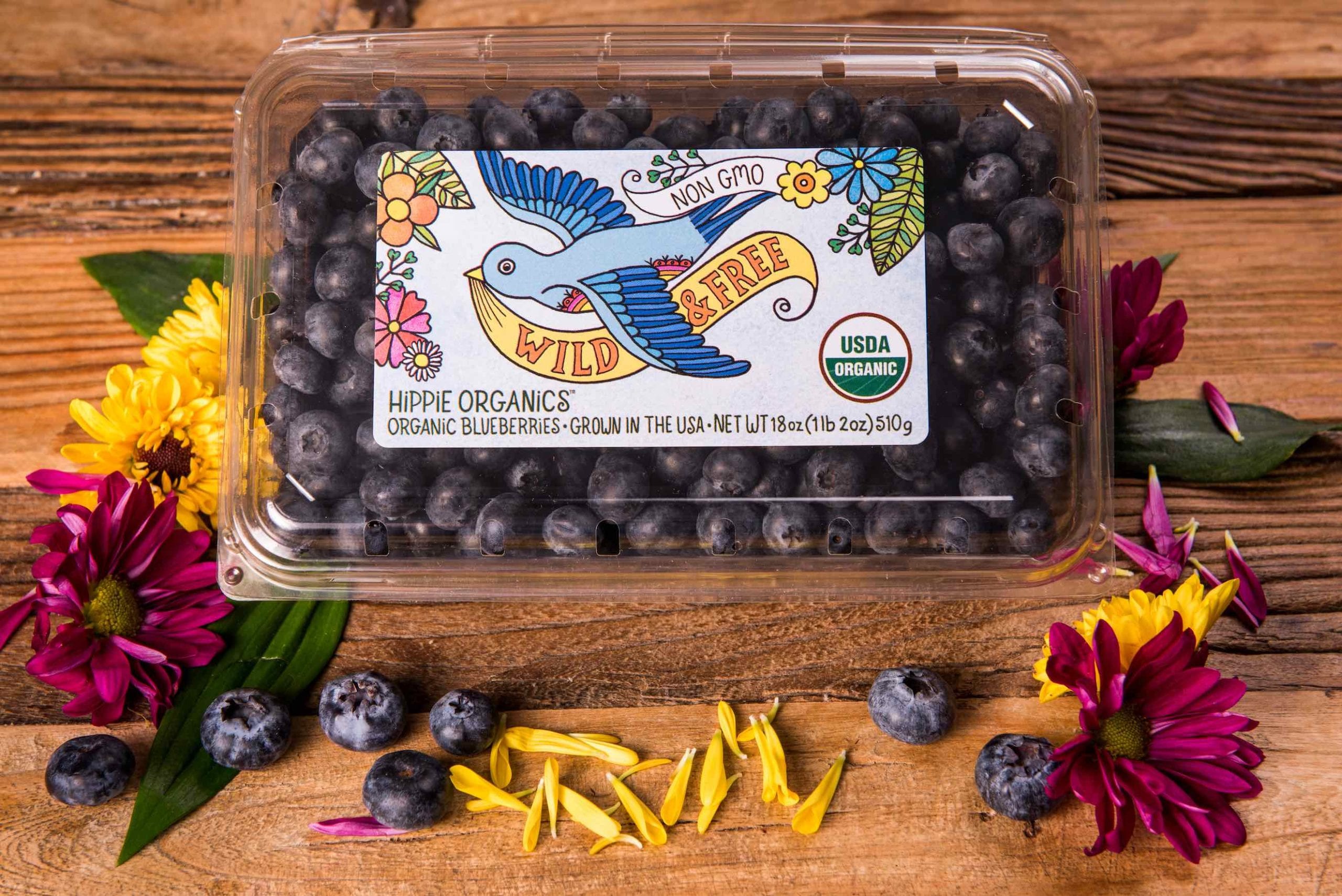 Aerial closeup view of package of organic blueberries surrounded by flowers