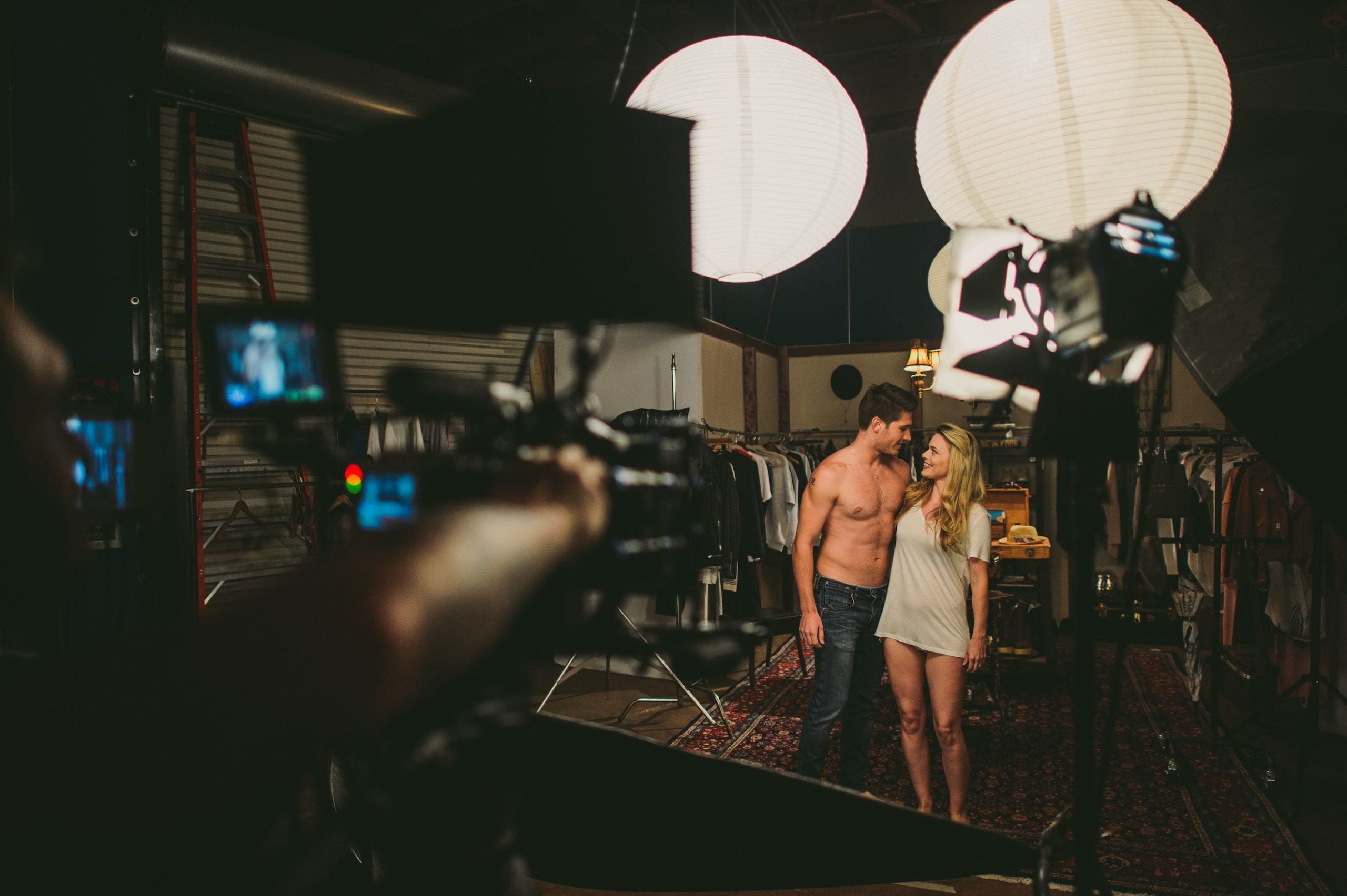AllSaints Clothing brand Behind the scenes look at a shirtless man with a woman wearing a long gray t shirt being filmed by videographer in a studio