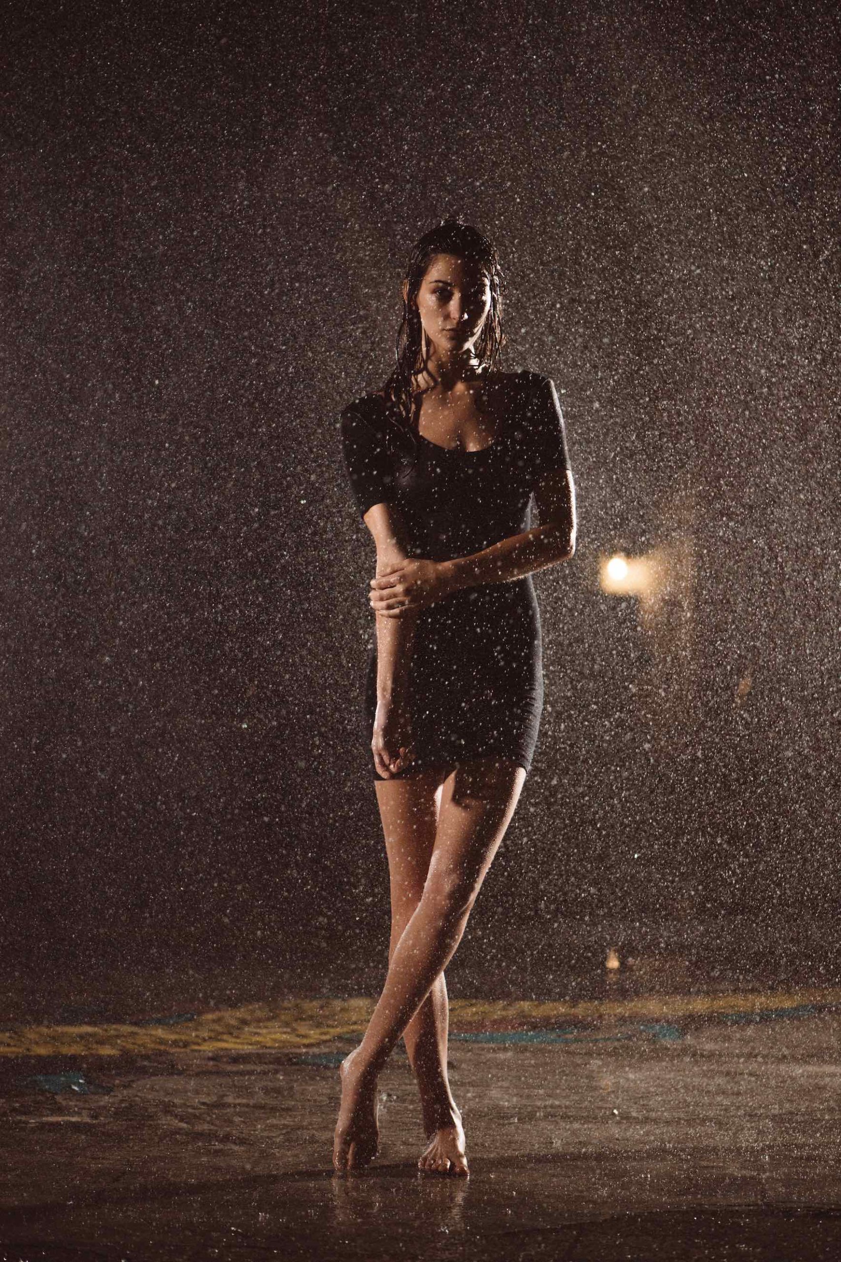 IU Woman with long hair posing for camera barefoot wearing a black dress under a shower of water